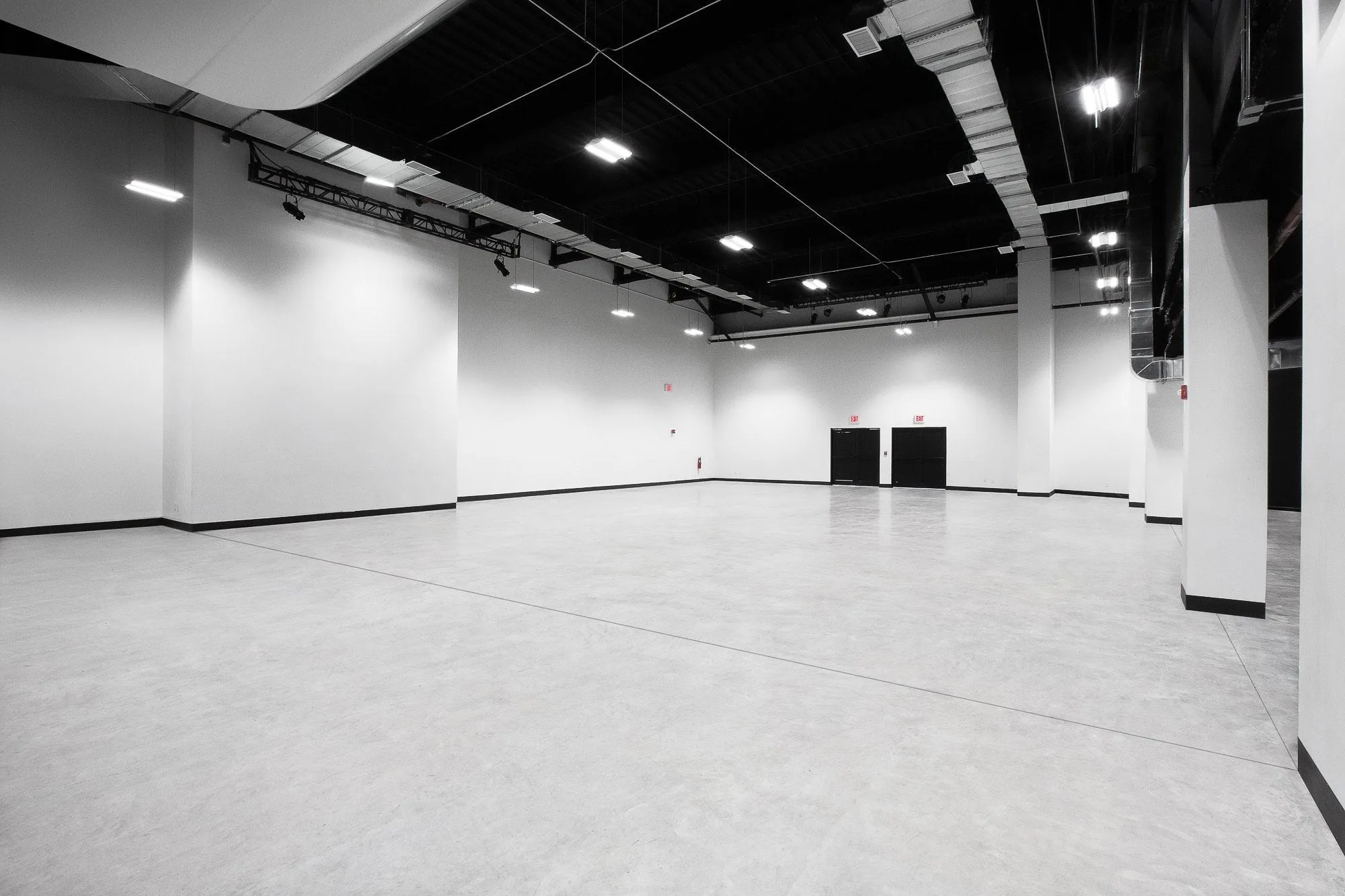 Empty white stage with grey floor, black ceiling, lighting truss and double black doors in Slate Studios Studio 2.
