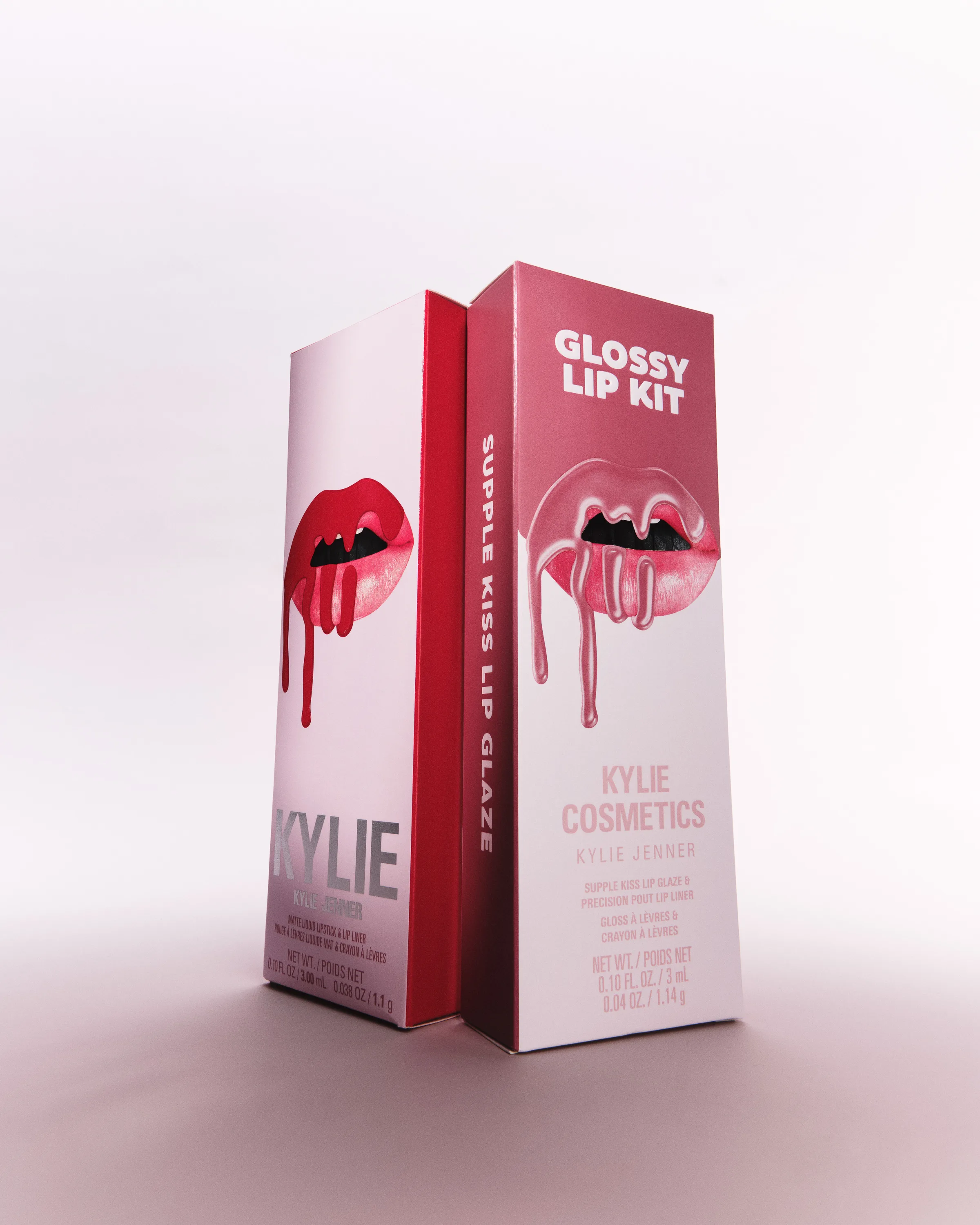 Two pink Glossy Lip Kit boxes with dripping lip artwork standing on a pale pink backdrop, for Kylie Cosmetics.