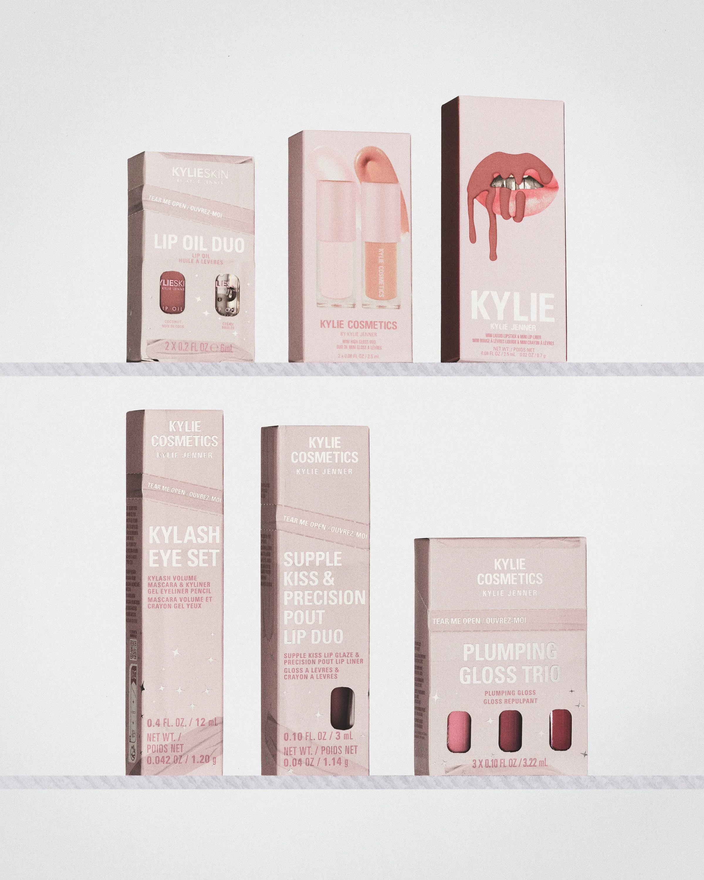 Pink holiday gift set boxes, including lip oil duo, Kylash eye set and plumping gloss trio, on two shelves, for Kylie Cosmetics.