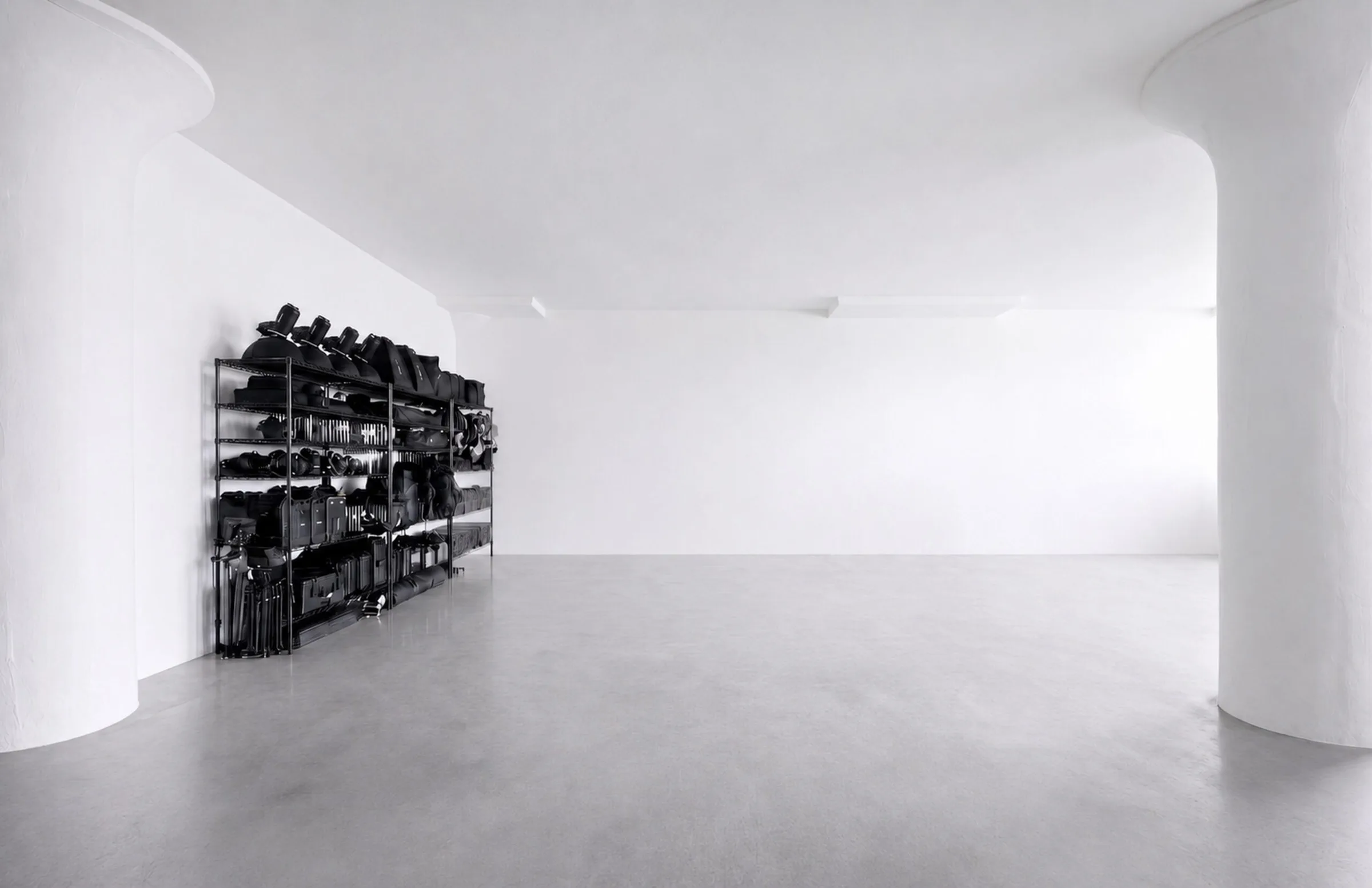 White studio with concrete floor, round pillars and black shelves of lighting gear at Studio 1 in Long Island City.