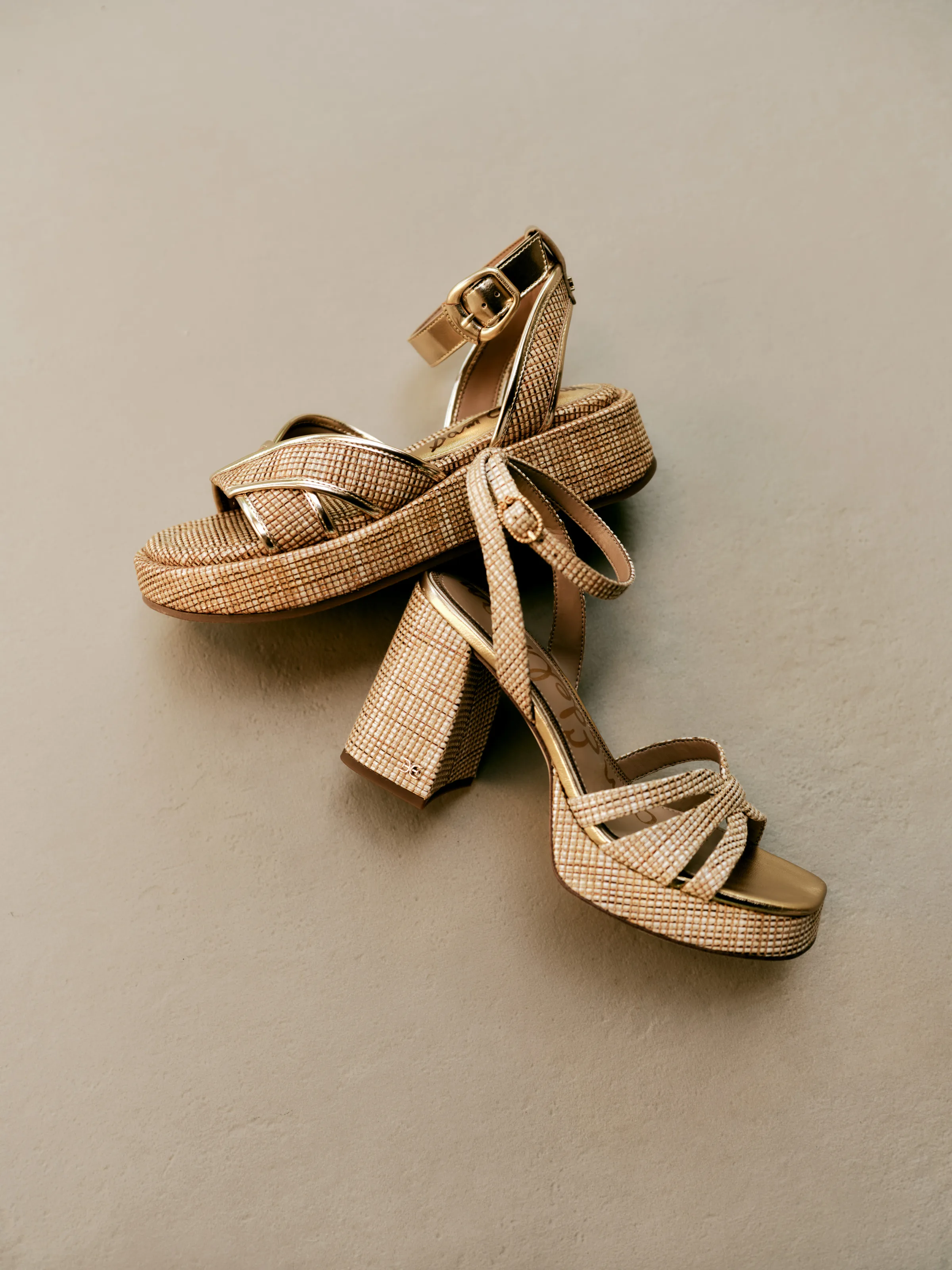 Pair of woven raffia platform sandals with gold straps and block heels on a taupe backdrop, for Sam Edelman.