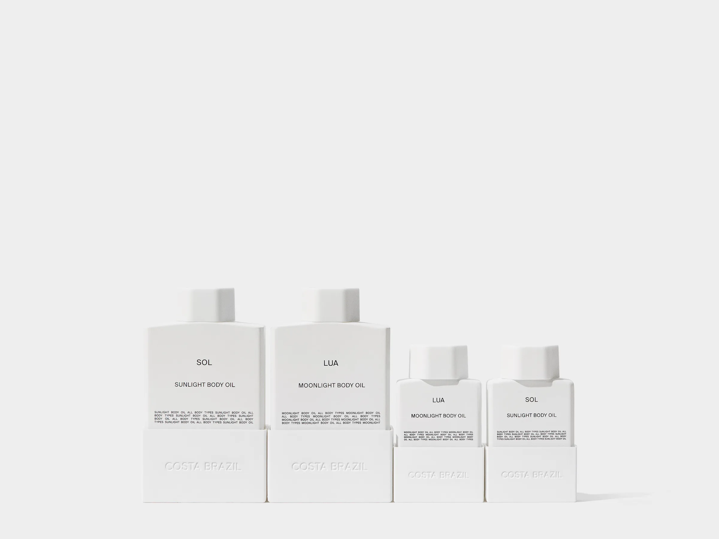 Four white Sol and Lua body oil bottles in two sizes lined up on a plain white background, for Costa Brazil.