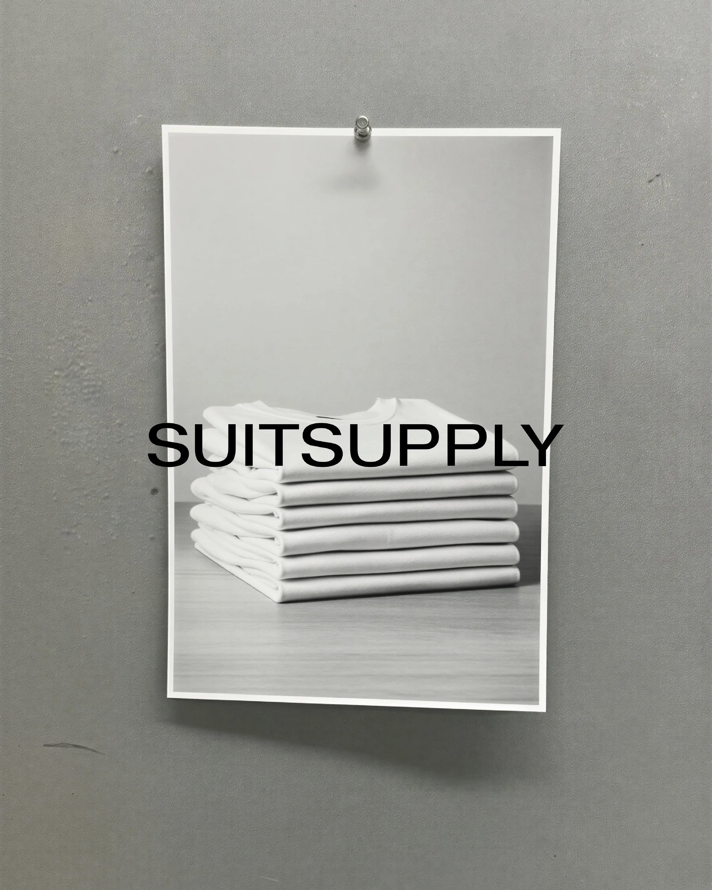 AI image of a pinned print showing a stack of folded white T-shirts on a grey wall, with the brand name overlaid. Suitsupply AI Concept.