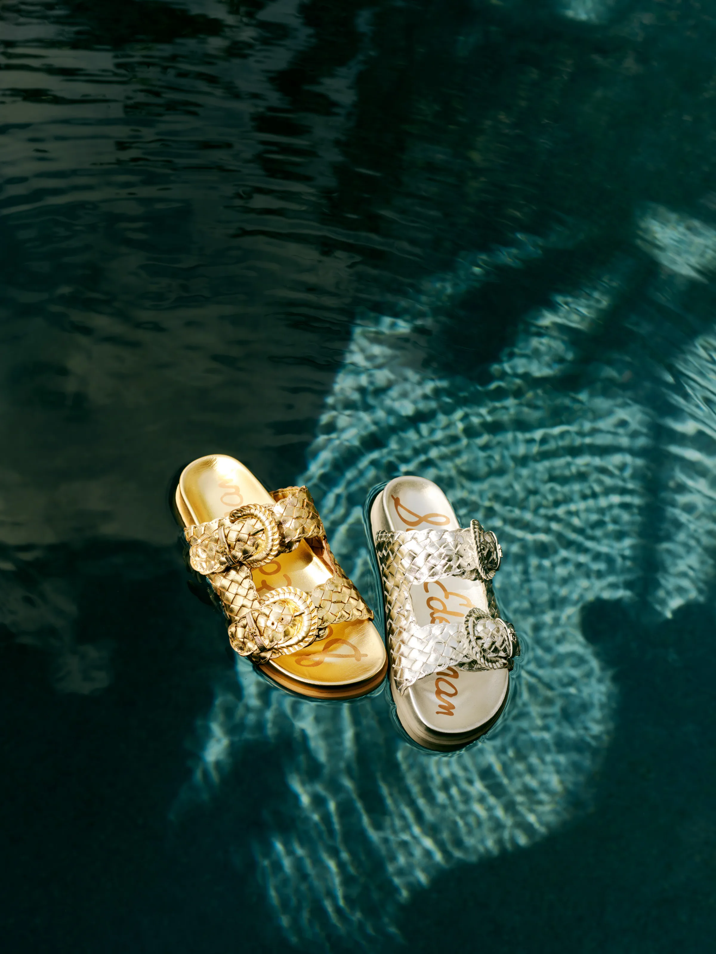 Gold and silver woven buckle slide sandals floating on dark rippling pool water, for Sam Edelman.