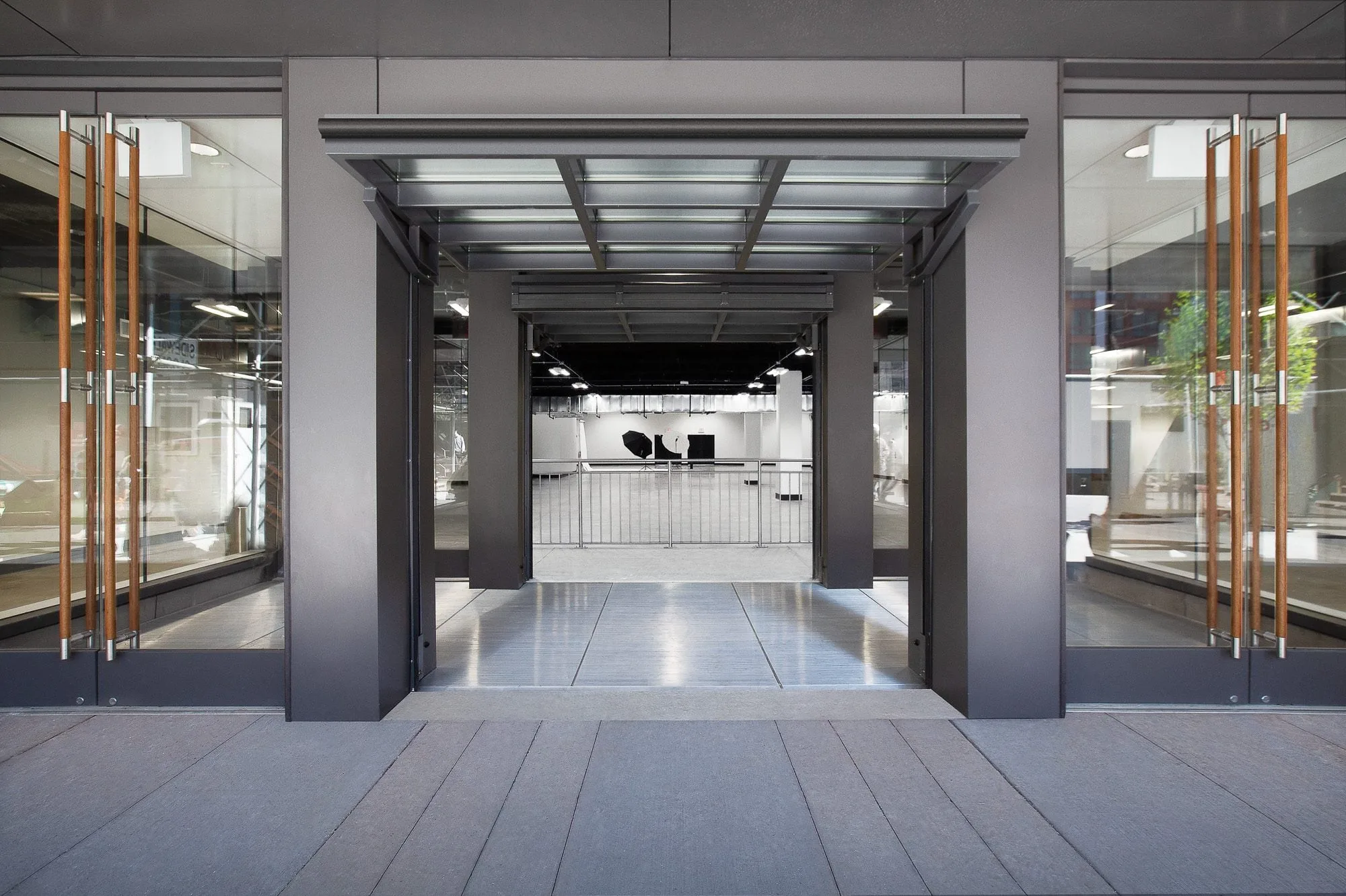 Glass double-door entrance with wood handles opening onto a white stage with lighting gear at Slate Studios Studio 2.