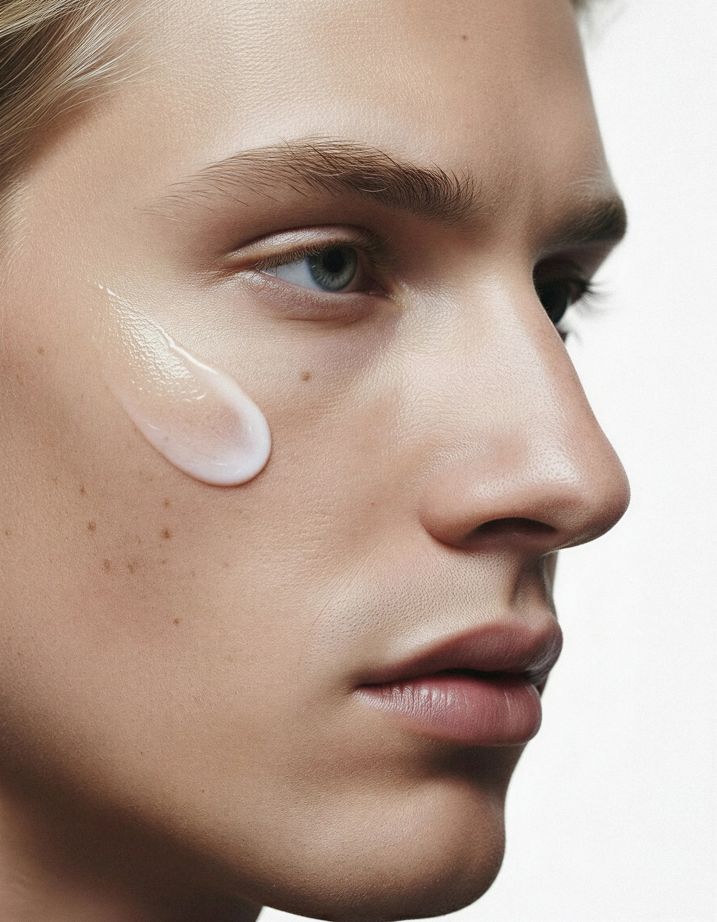 AI image of a man's face in profile with a swipe of white skincare cream on his cheek. Typology AI Concept.