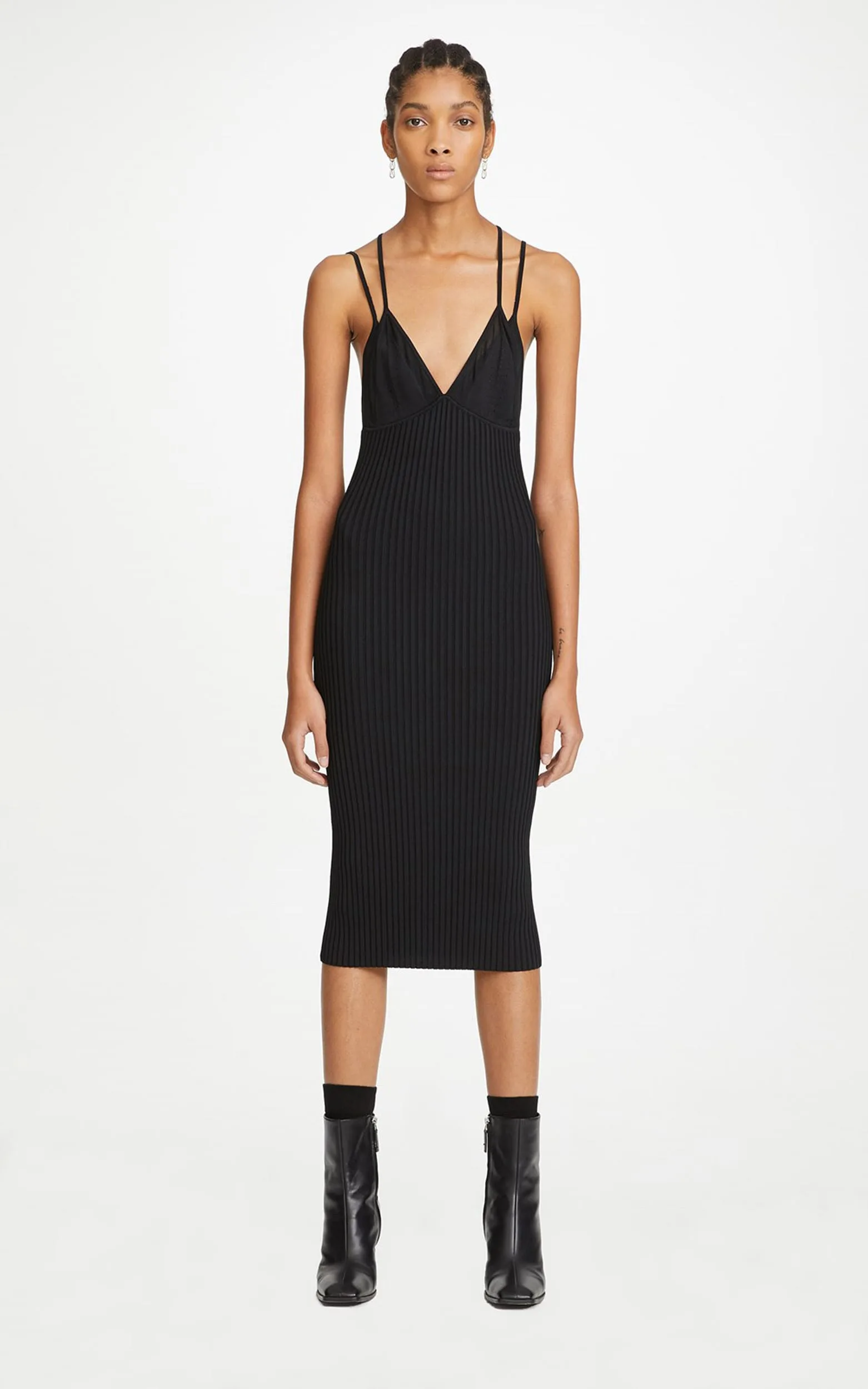 Model in a black ribbed knit midi slip dress with double straps and black ankle boots on white, for Dion Lee.