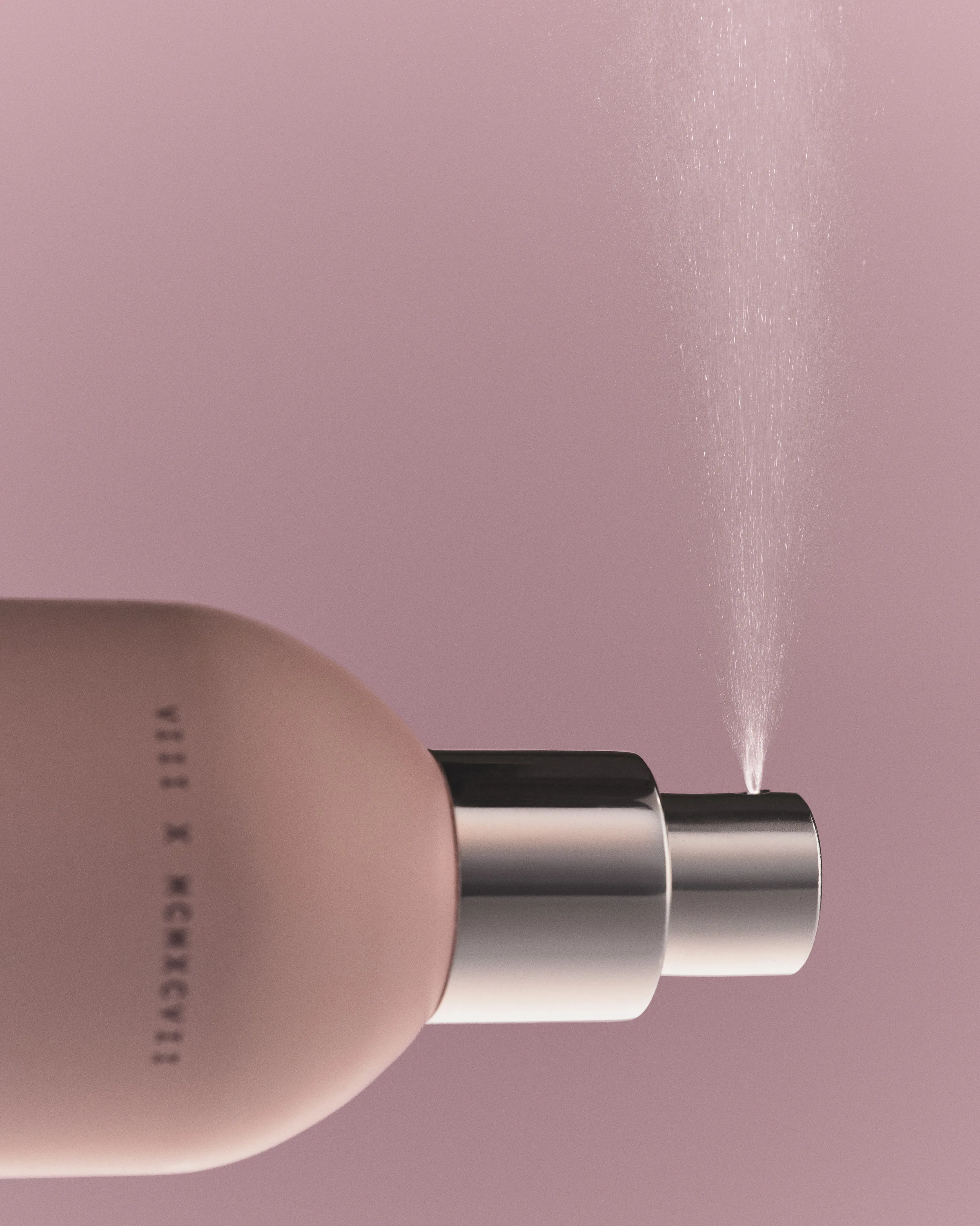 Pink hair and body mist bottle with silver nozzle releasing a fine spray against a mauve backdrop, for Kylie Cosmetics.
