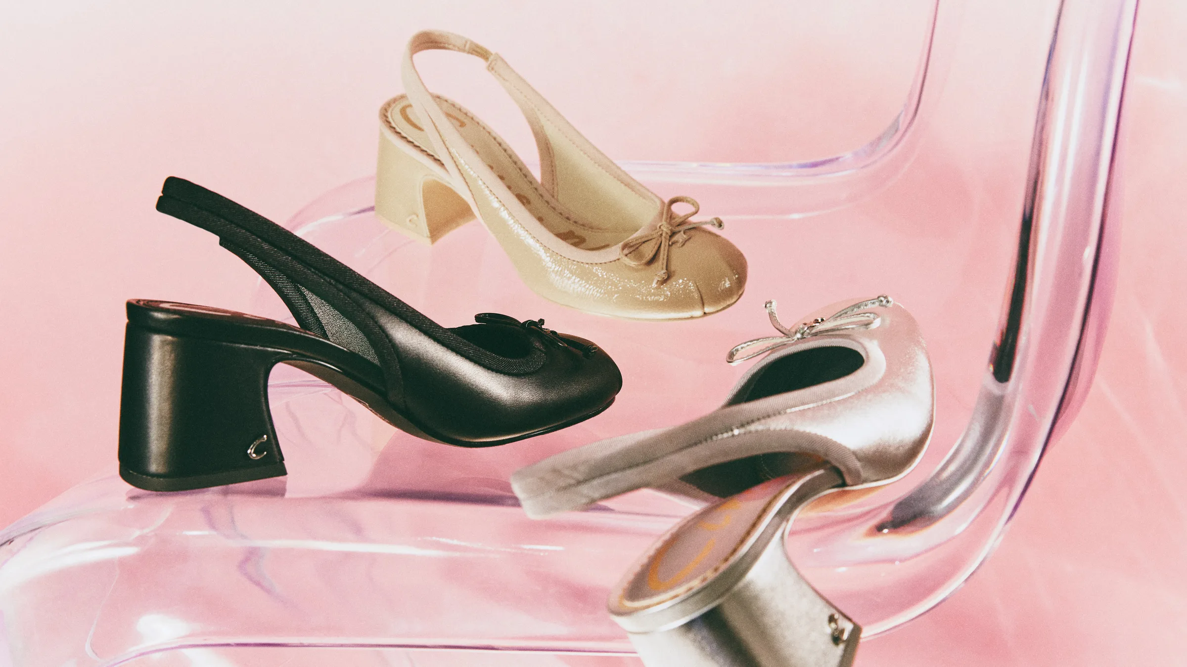 Black, vanilla and silver slingback heels with bows arranged on a clear acrylic chair against pink, for Sam Edelman.