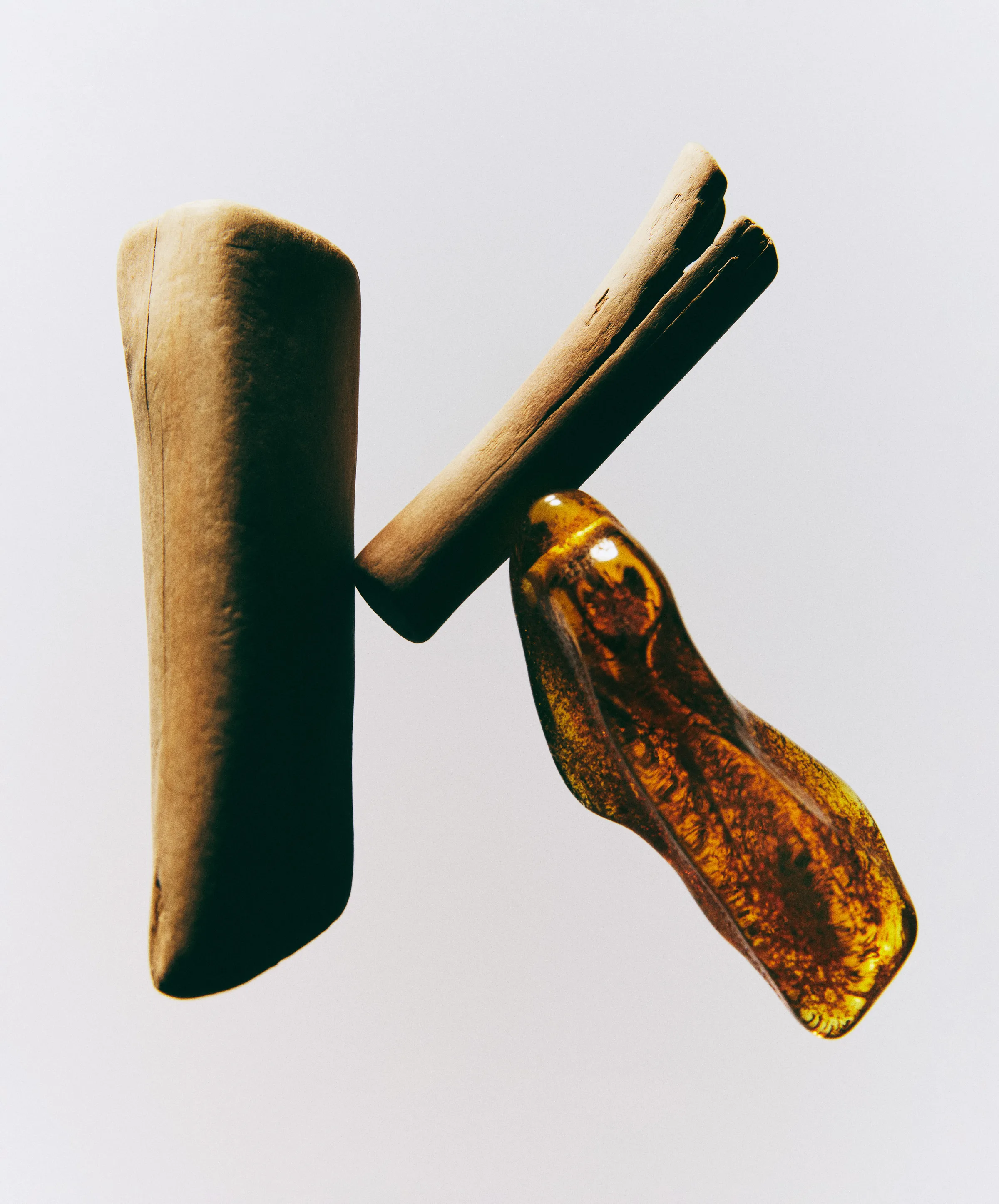 Still life of driftwood and amber resin forming the letter K on a grey background, showing fragrance base notes, for Kylie Cosmetics.