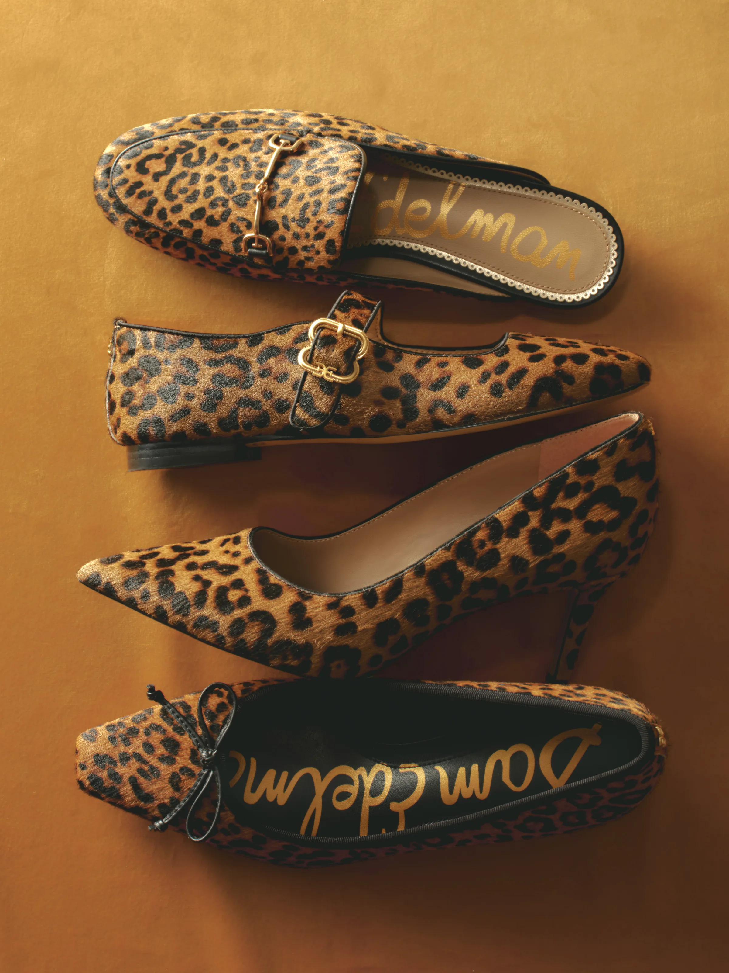 Four leopard-print calf hair shoes—mule, Mary Jane flat, pump and bow flat—laid on a mustard velvet backdrop, for Sam Edelman.