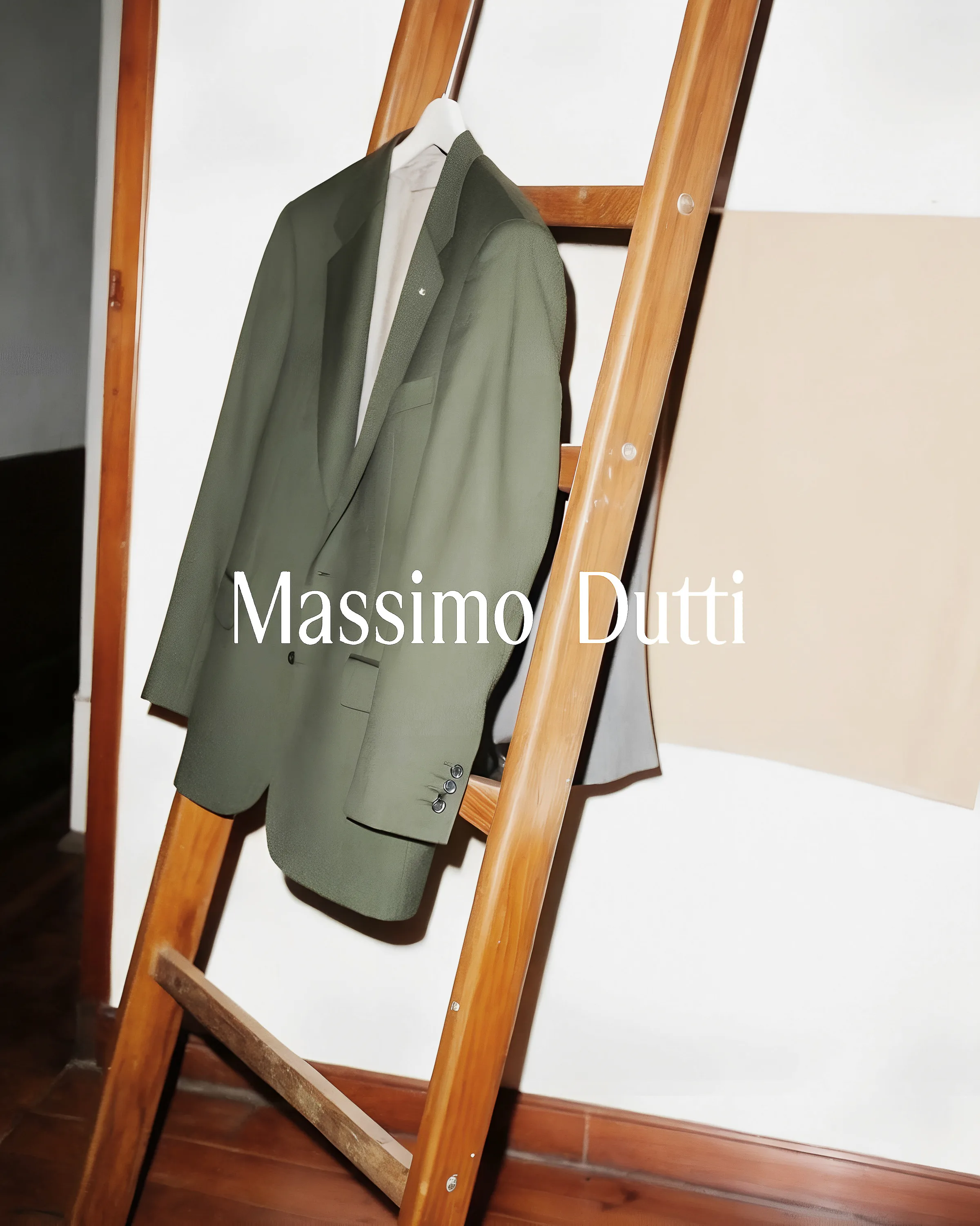 Olive green blazer hanging on a wooden ladder against a white wall, with the brand name overlaid. Massimo Dutti AI Concept.