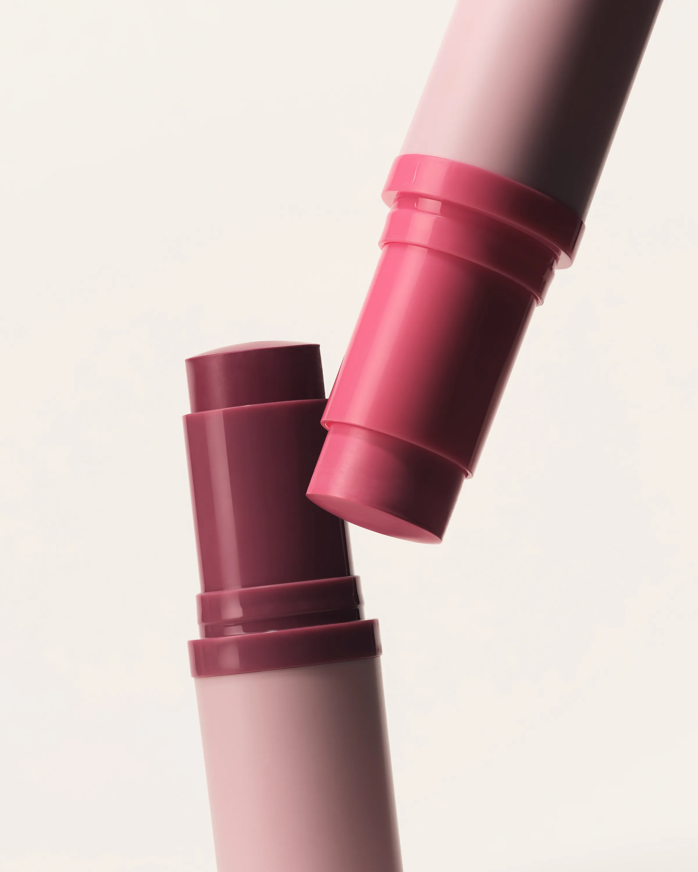 Two uncapped lip and cheek sticks in berry and pink shades meeting at an angle on a cream background, for Kylie Cosmetics.
