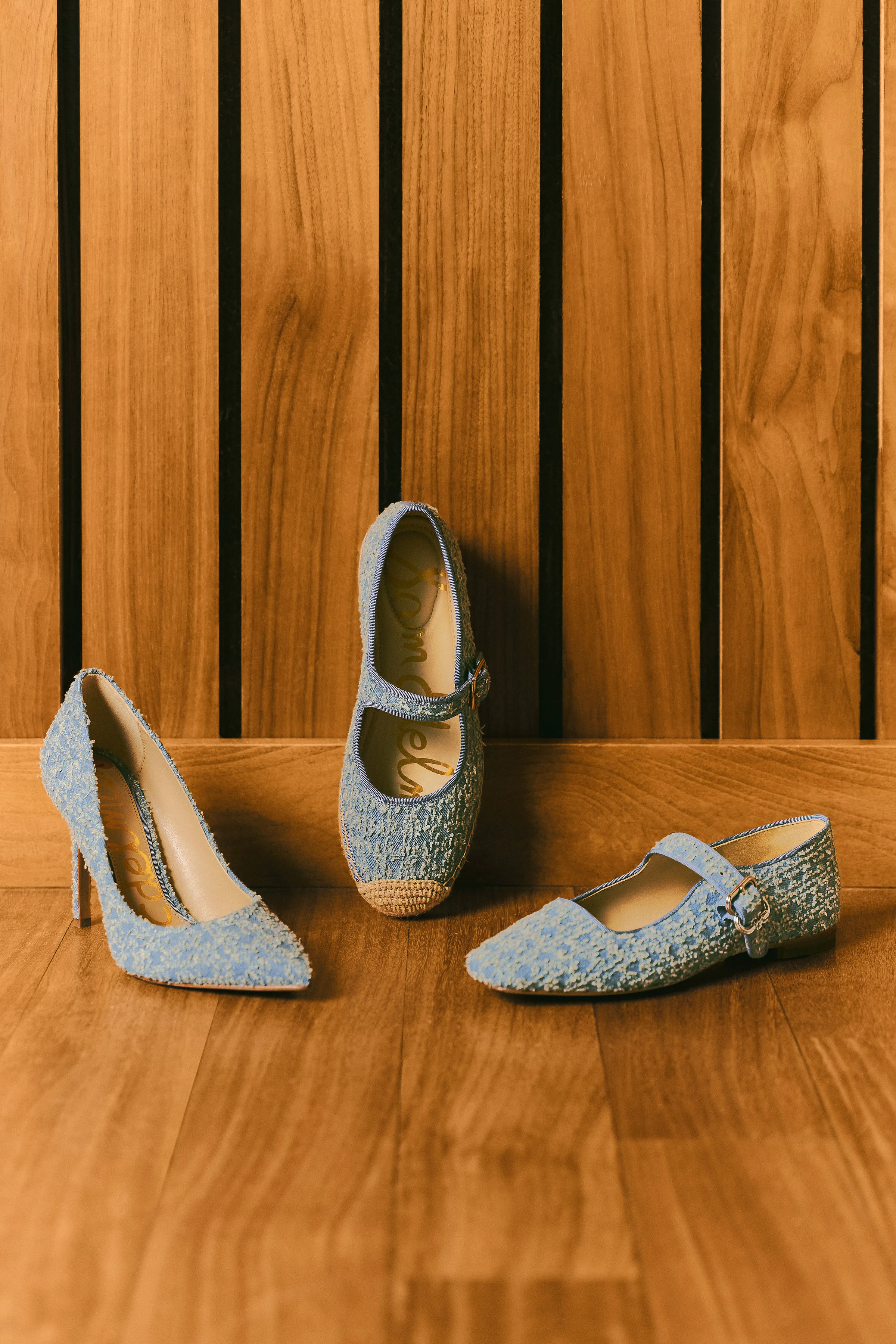 Light blue tweed pump, espadrille Mary Jane and buckle flat on a wood floor against slatted wood panels, for Sam Edelman.