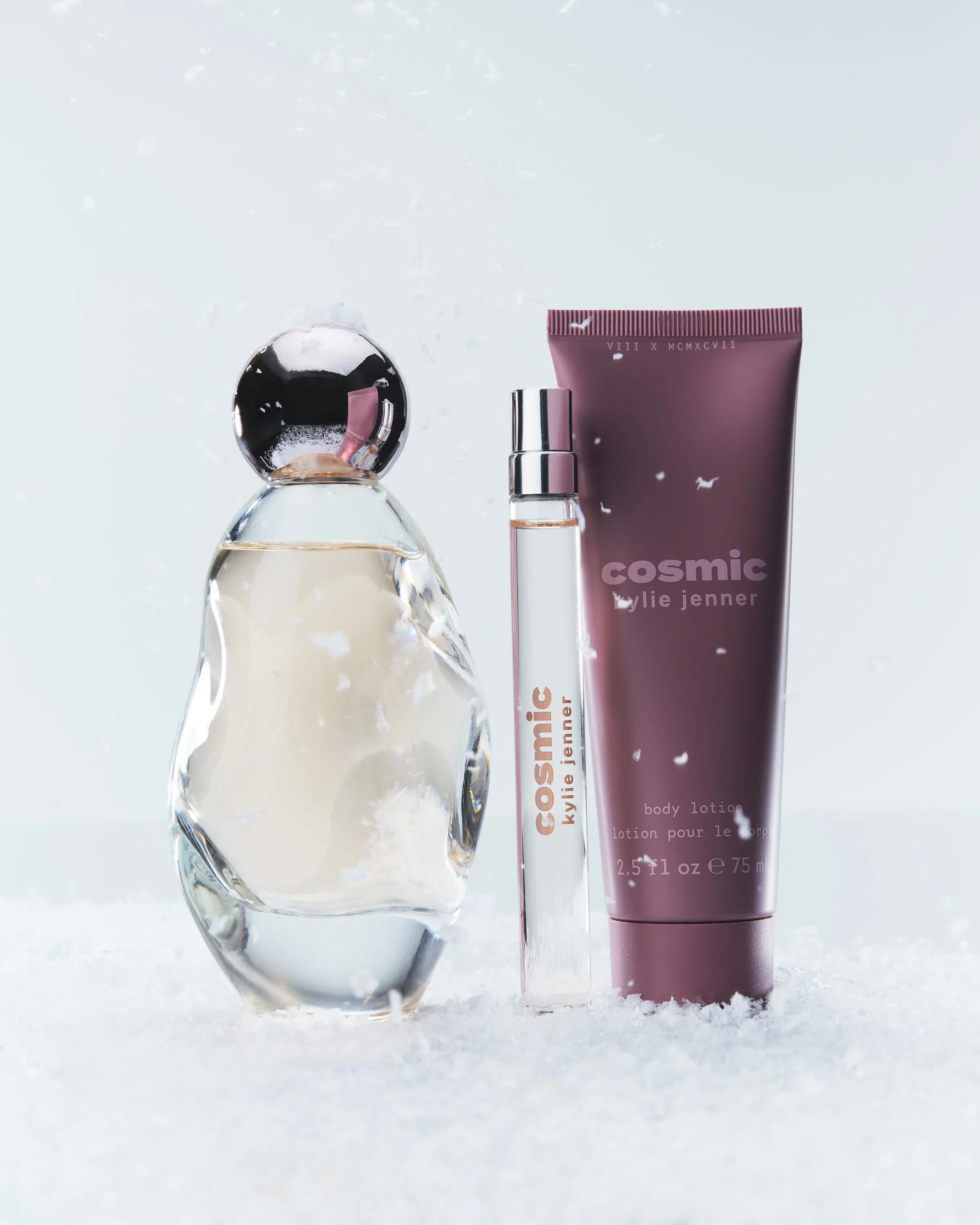 Cosmic perfume bottle, pen spray and plum body lotion tube standing in falling snow, for Kylie Cosmetics.