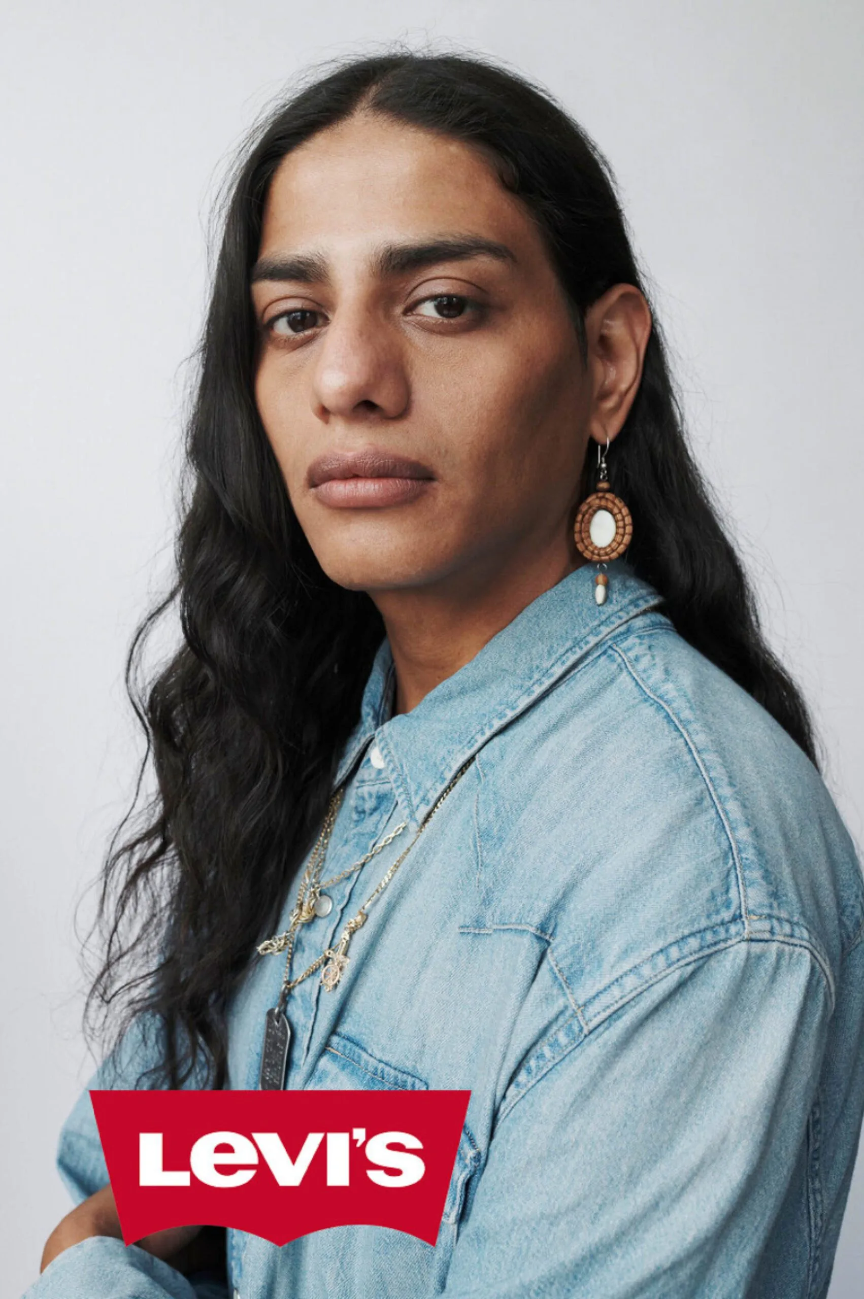 Portrait of a model with long dark wavy hair in a light denim shirt, beaded earring and layered necklaces, for Levi's.