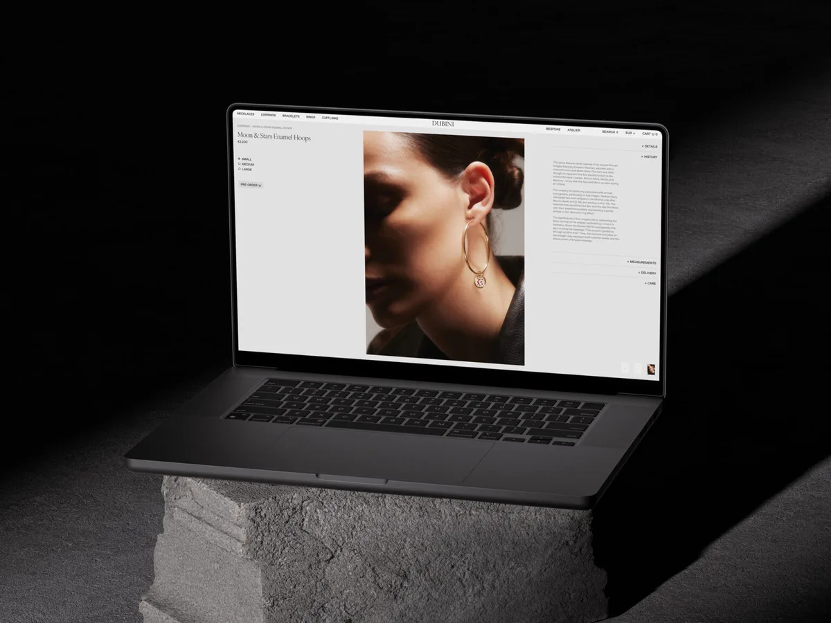 Laptop on a concrete block showing a product page with a model wearing gold Moon & Stars hoop earrings, for Dubini.