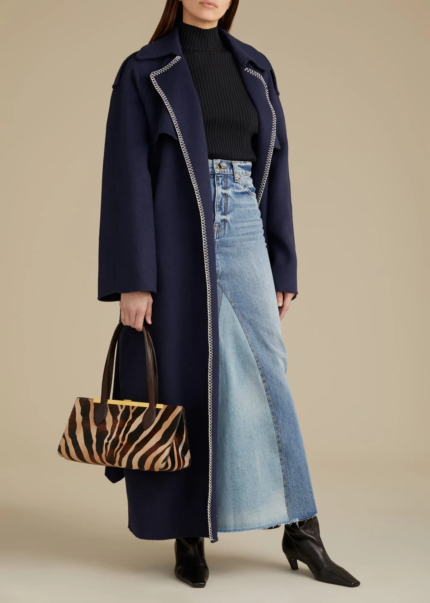 Model in a navy whipstitched wool coat, long patchwork denim skirt and black boots, holding a zebra-print bag, for Khaite.