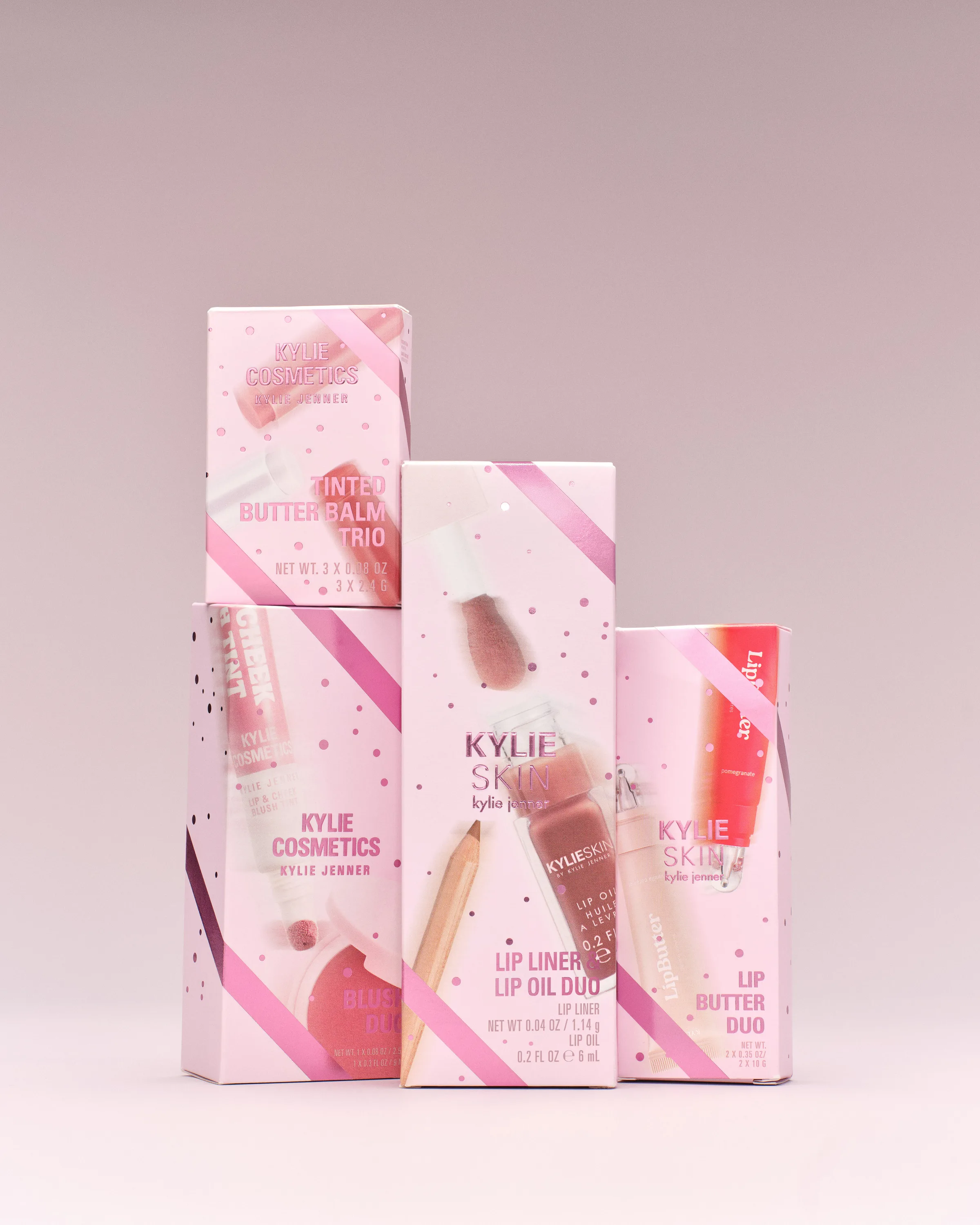 Pink holiday gift set boxes stacked on a mauve backdrop, including lip oil and butter balm duos, for Kylie Cosmetics.