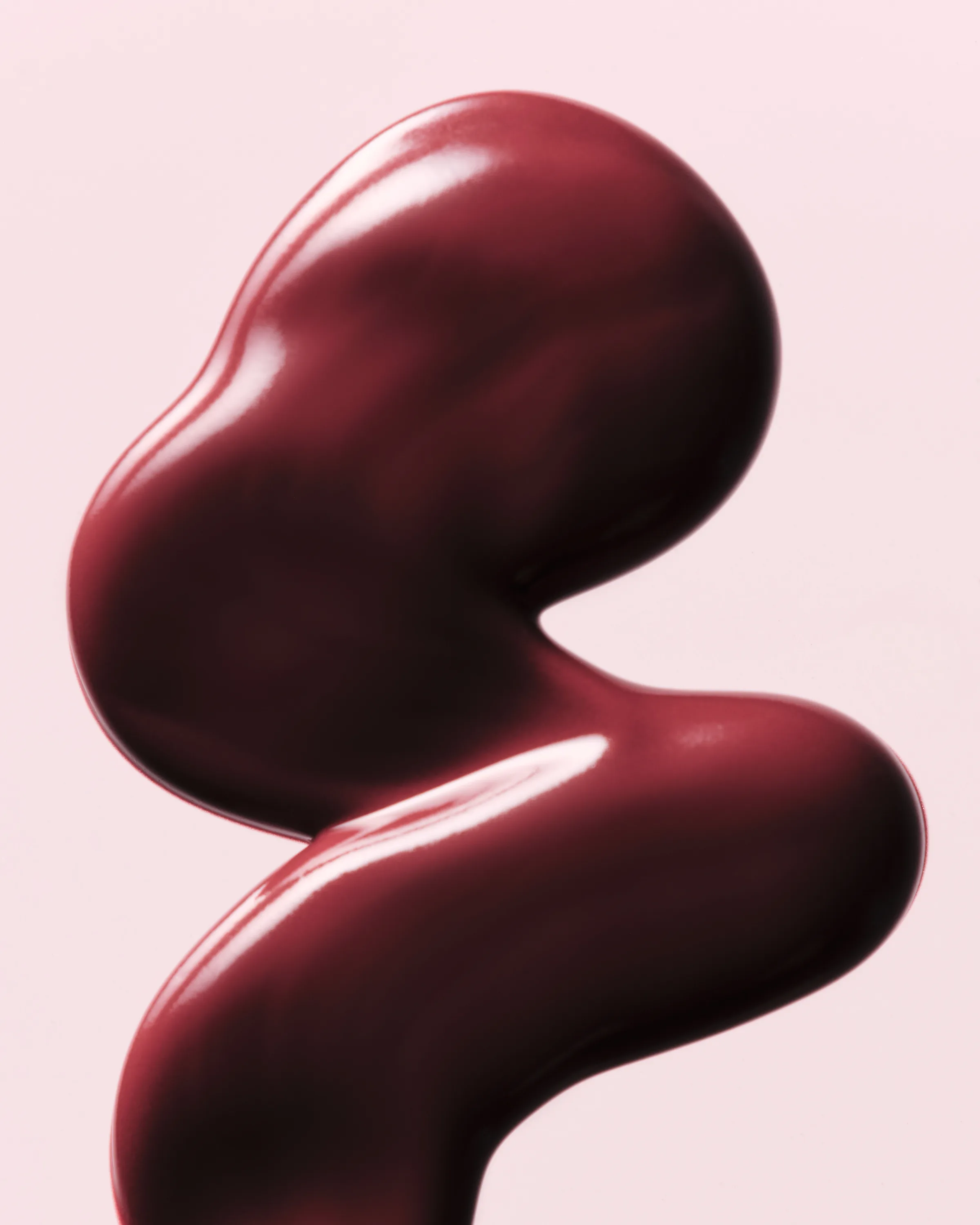 Glossy berry-red lip product swatch in a curving sculptural shape on a pale pink background, for Kylie Cosmetics.