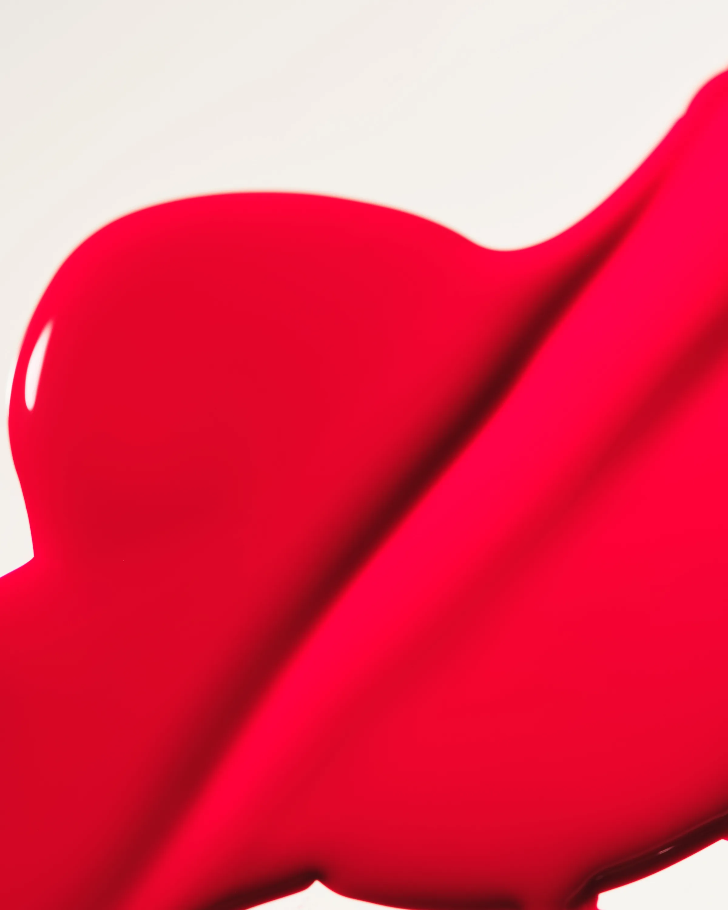 Close-up swatch of glossy scarlet red nail lacquer spread across a white surface, for Kylie Cosmetics.