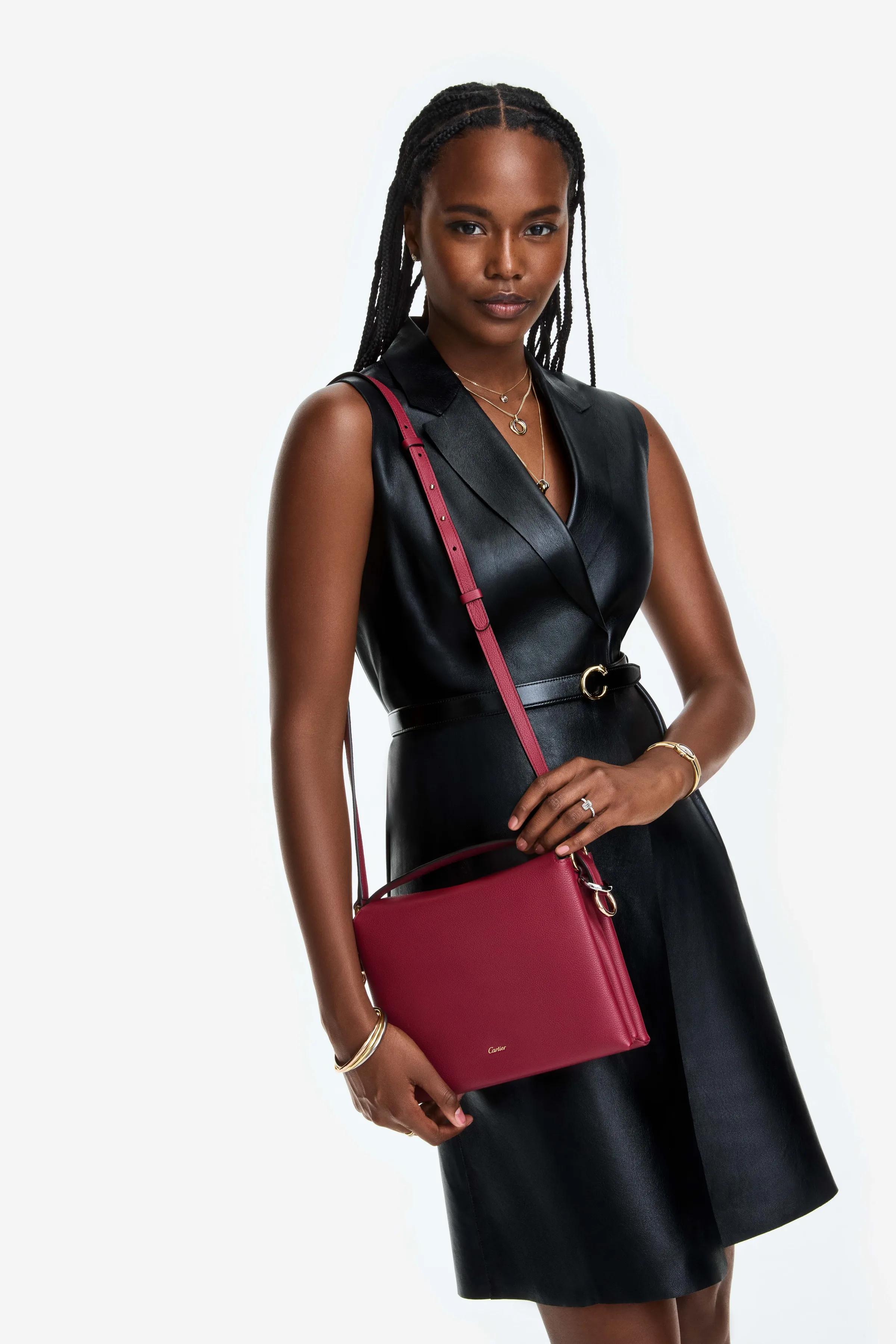 Model in a black leather sleeveless dress carrying a raspberry red leather crossbody bag on white, for Cartier.