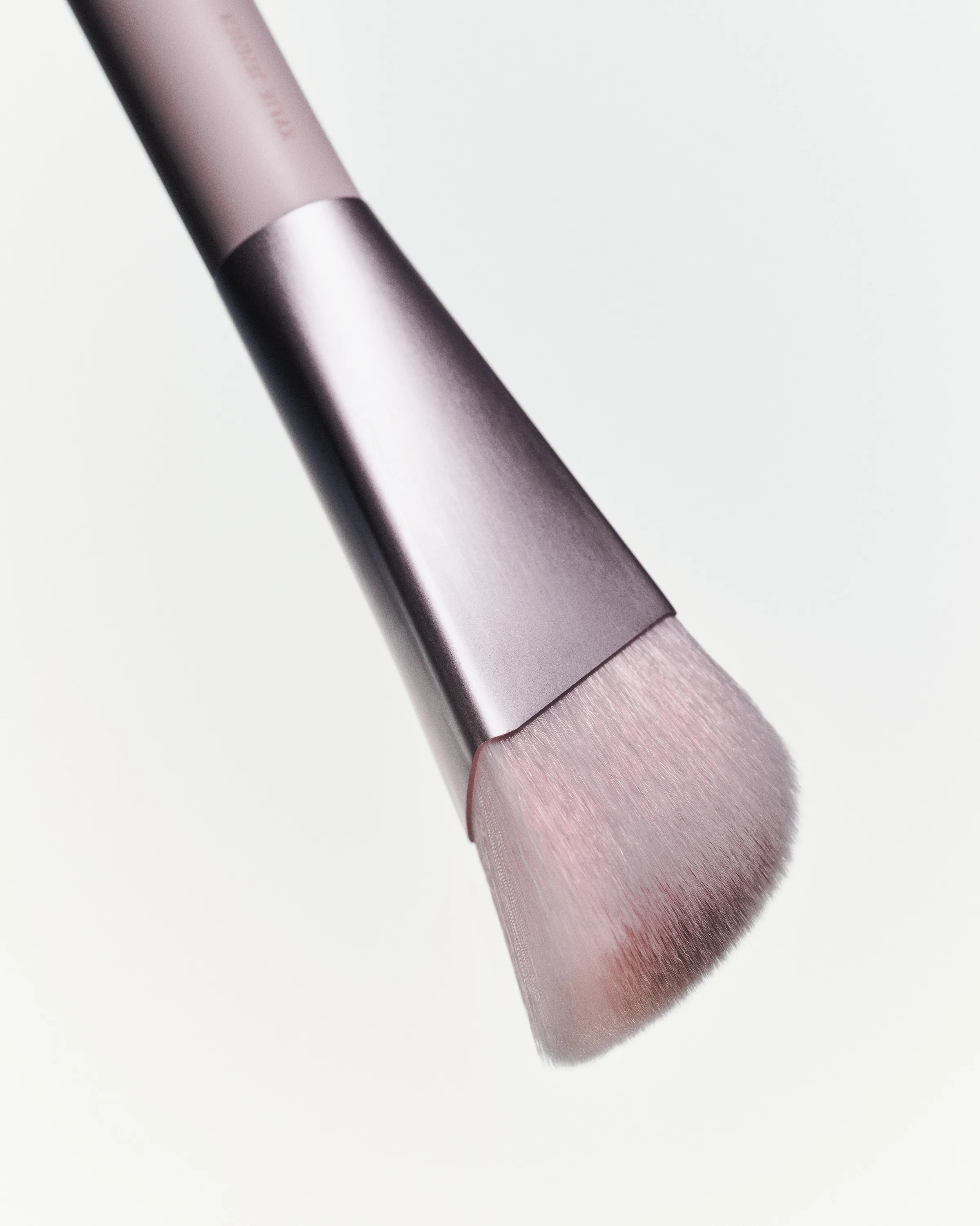 Close-up of an angled makeup brush with a mauve handle and metallic ferrule on a pale background, for Kylie Cosmetics.