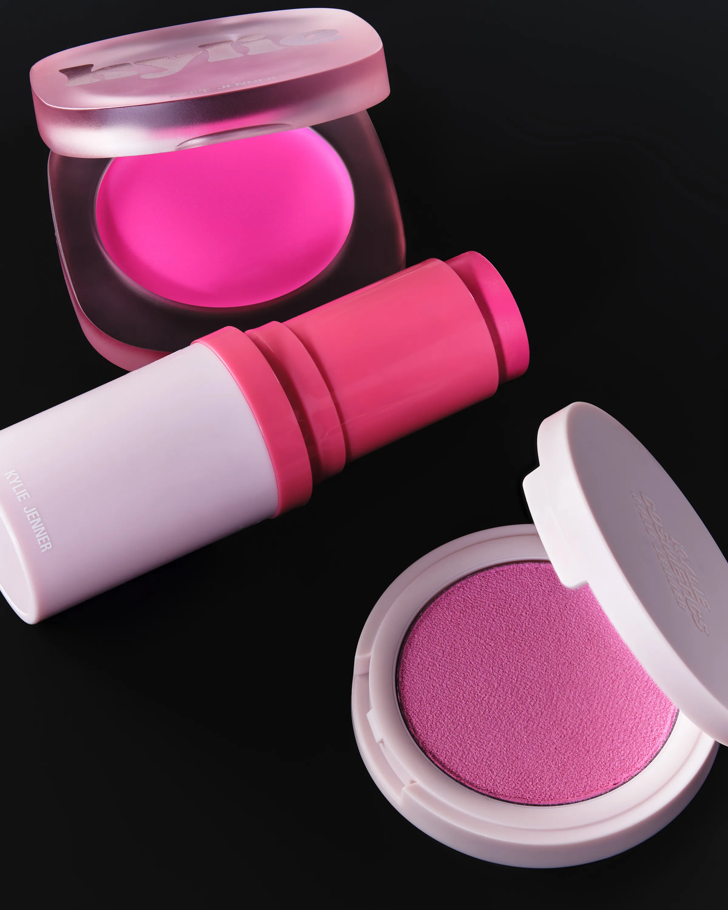 Still life of pink glow balm, blush stick and powder blush compacts on a black background, for Kylie Cosmetics.