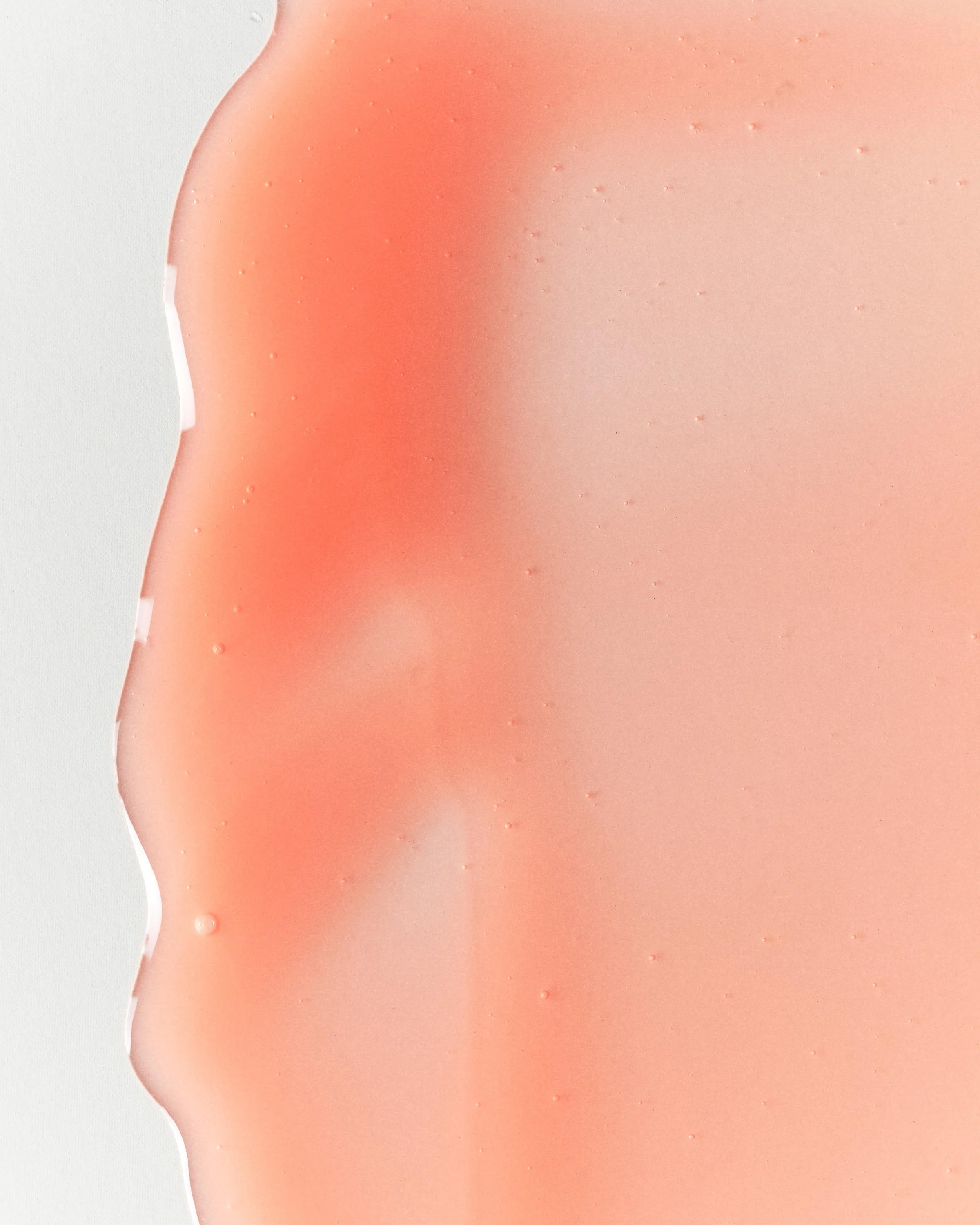 Close-up texture swatch of translucent peach-pink lip gloss smeared across a white surface, for Kylie Cosmetics.