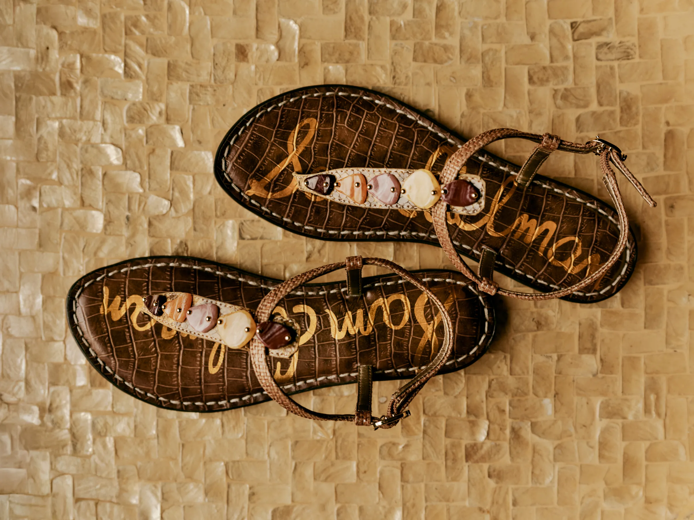 Brown croc-embossed thong sandals with polished stone details on a mother-of-pearl tile surface, for Sam Edelman.