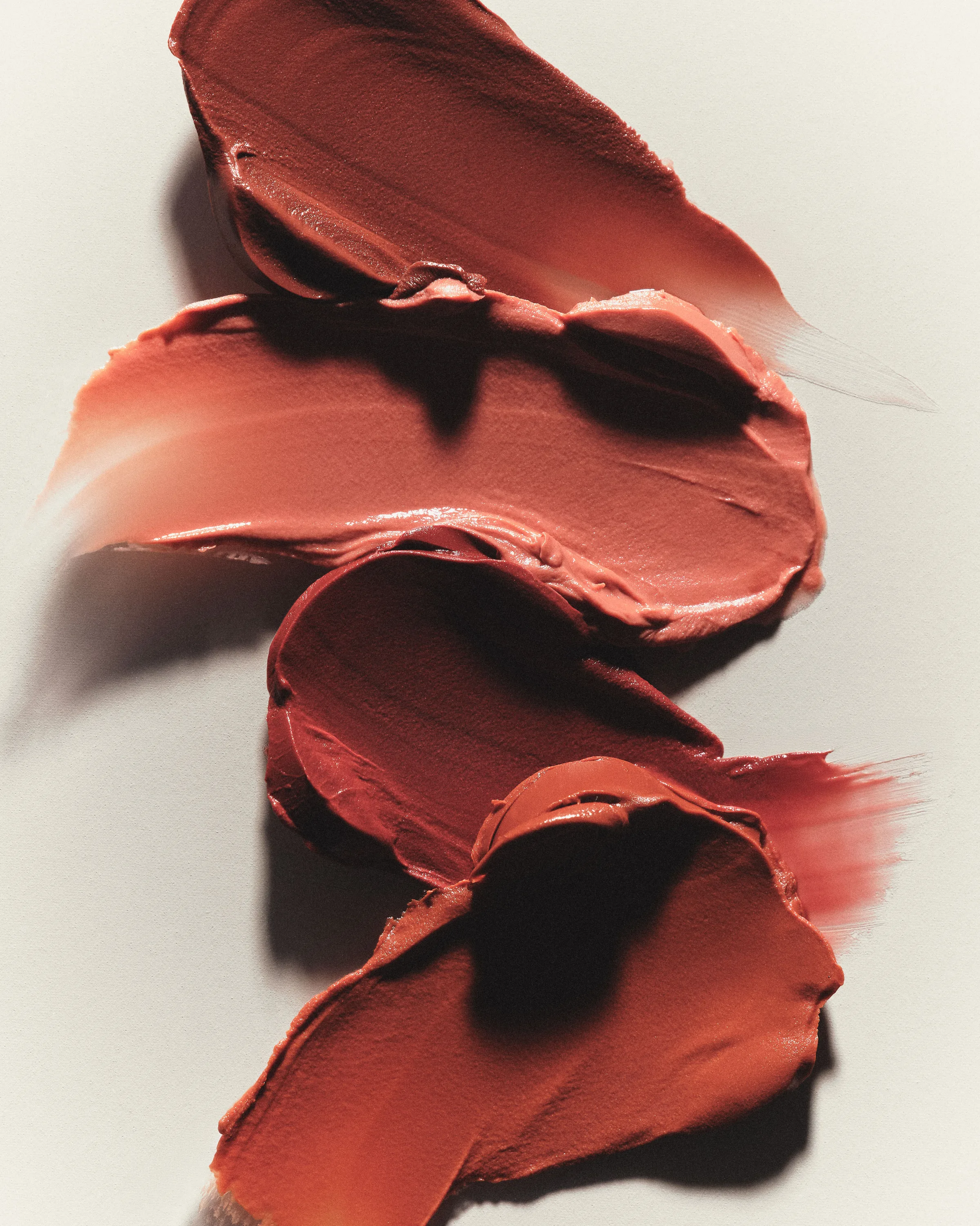 Four smeared swatches of terracotta and brick-red lip cream on a cream background, for Kylie Cosmetics.