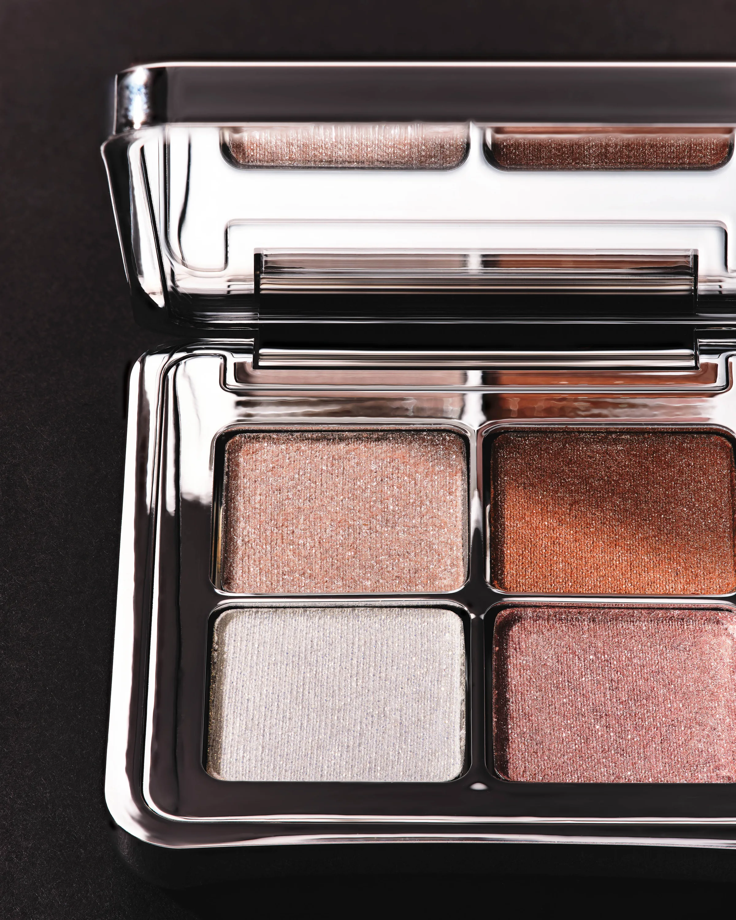 Open chrome eyeshadow quad with shimmering pink, copper, silver and mauve shades on a black surface, for Kylie Cosmetics.
