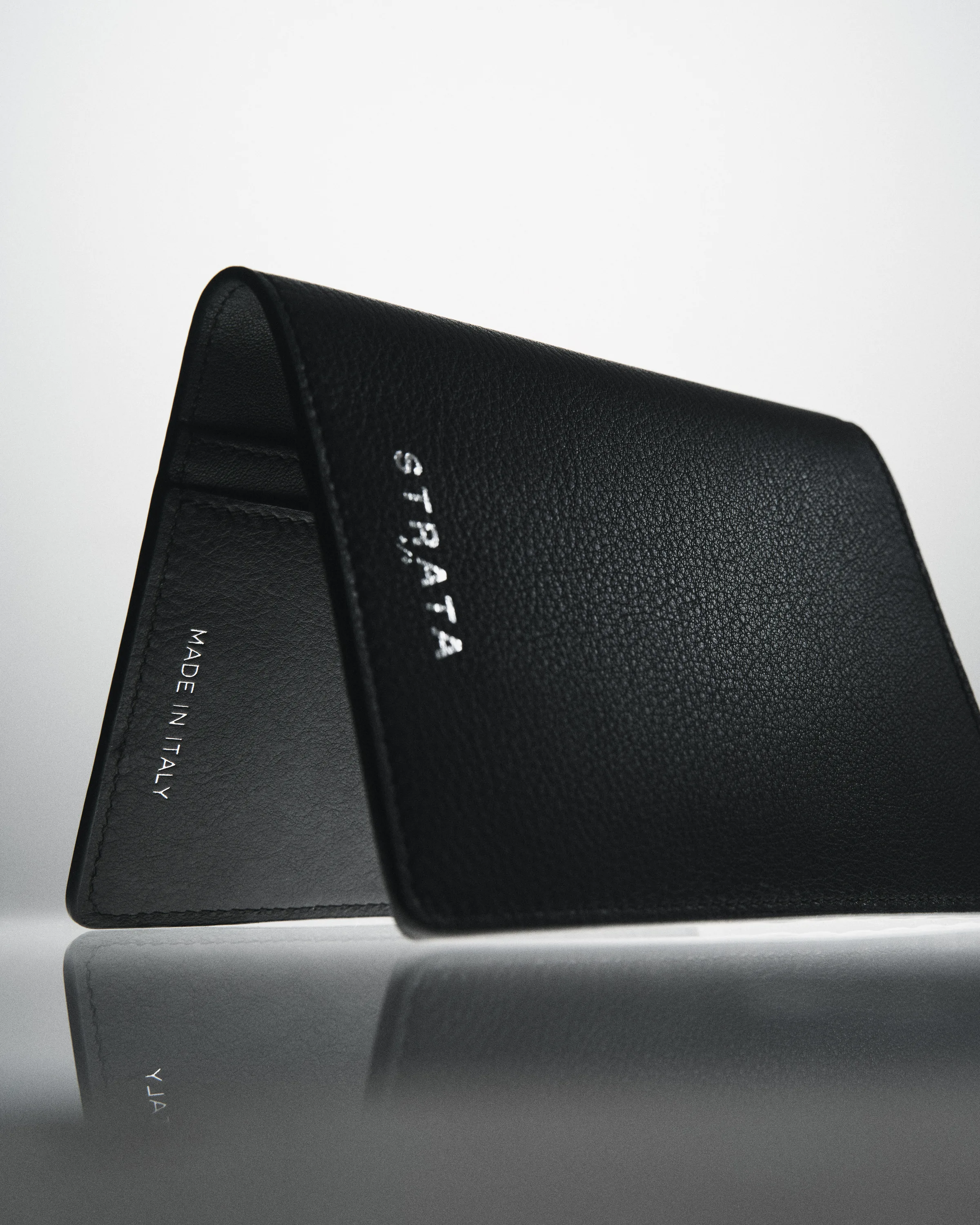 Black pebbled leather travel sleeve with silver Strata lettering, standing open on a reflective grey surface, for Strata.