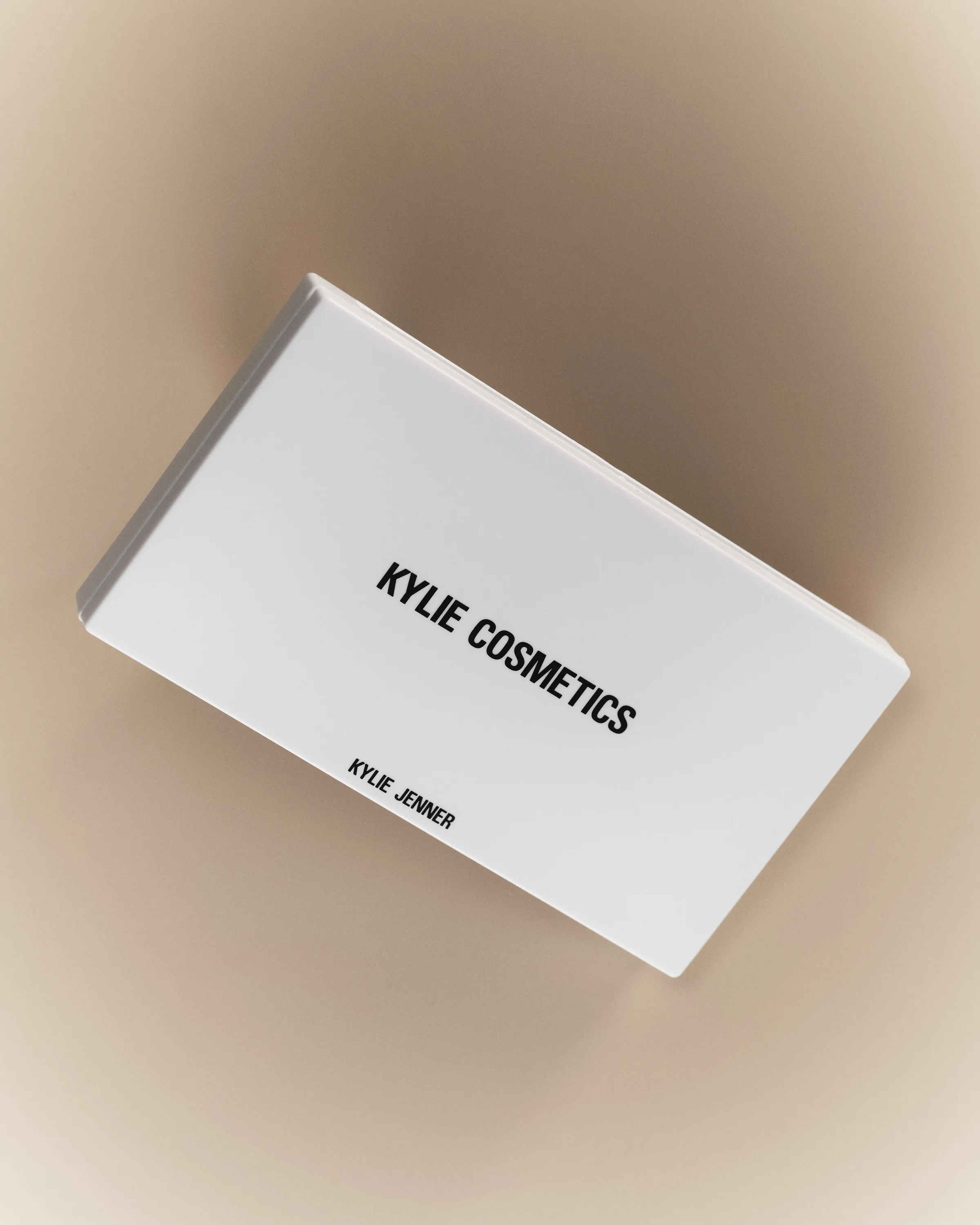 White eyeshadow palette case tilted against a soft beige fog background, for Kylie Cosmetics.