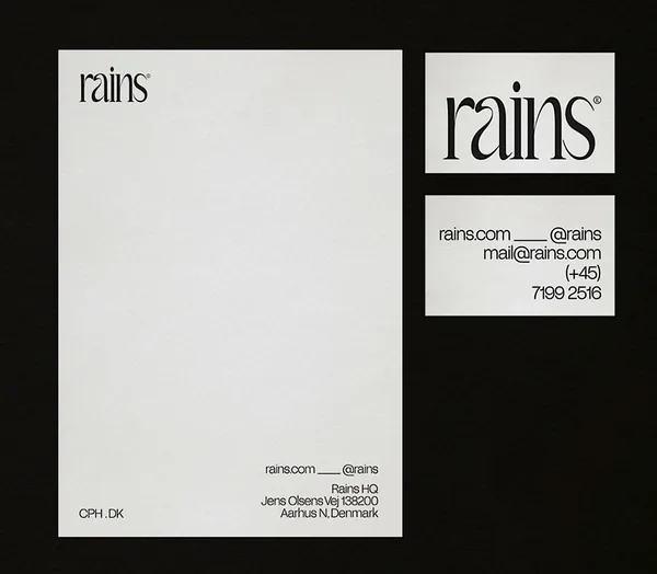 Letterhead and business card front and back with black serif wordmark on off-white paper over a black background, for Rains.