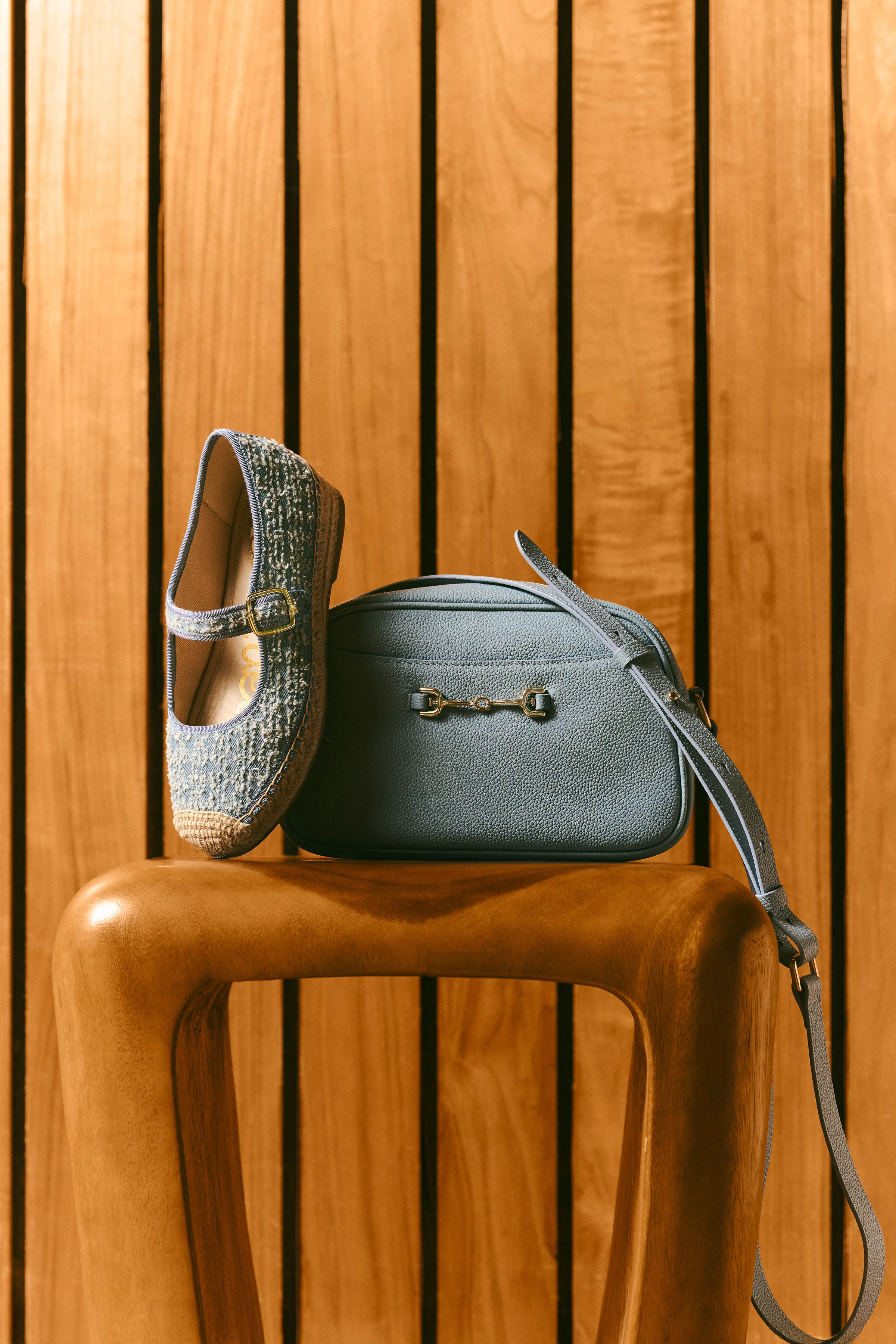 Blue tweed Mary Jane espadrille and pebbled leather crossbody bag on a wooden stool against slatted wood, for Sam Edelman.