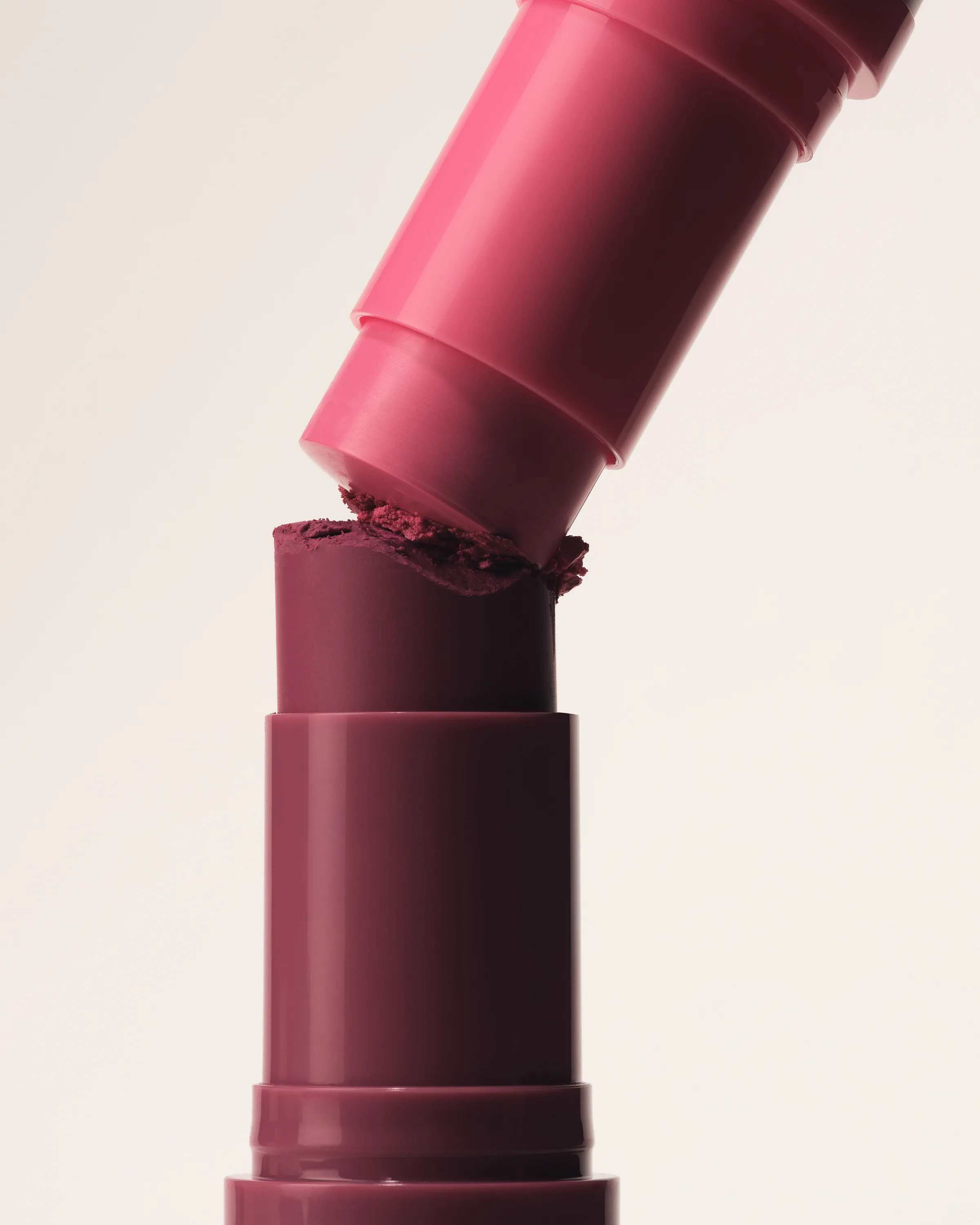 Pink lipstick tube pressing into a crumbling plum lipstick bullet against a cream backdrop, for Kylie Cosmetics.