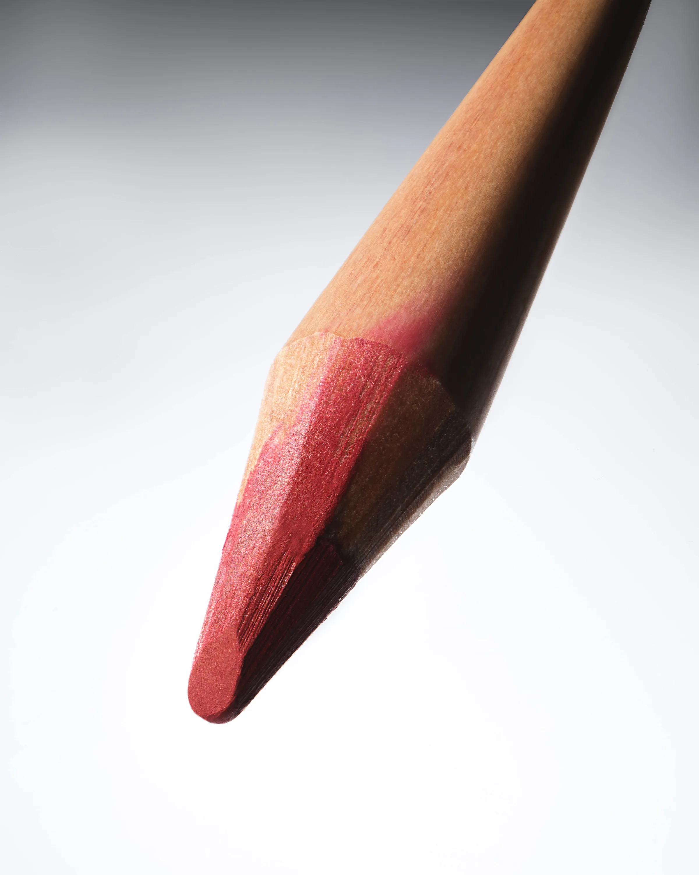 Close-up still life of a sharpened pink lip liner pencil tip with a wooden barrel on a grey gradient, for Kylie Cosmetics.