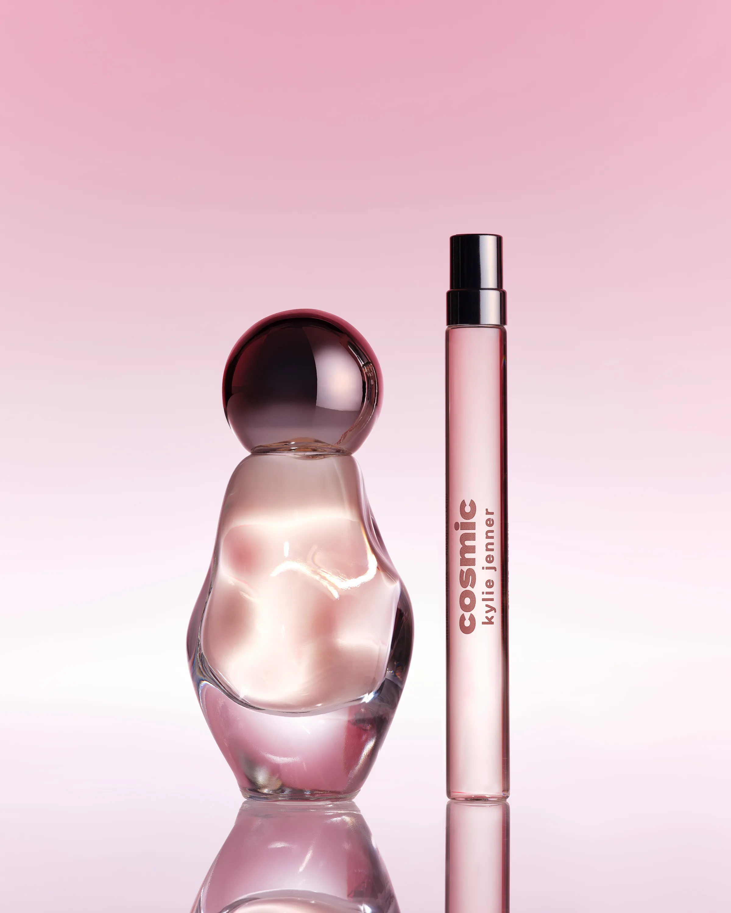 Cosmic eau de parfum bottle with orb cap beside a 10ml pen spray on a pink gradient with reflection, for Kylie Cosmetics.