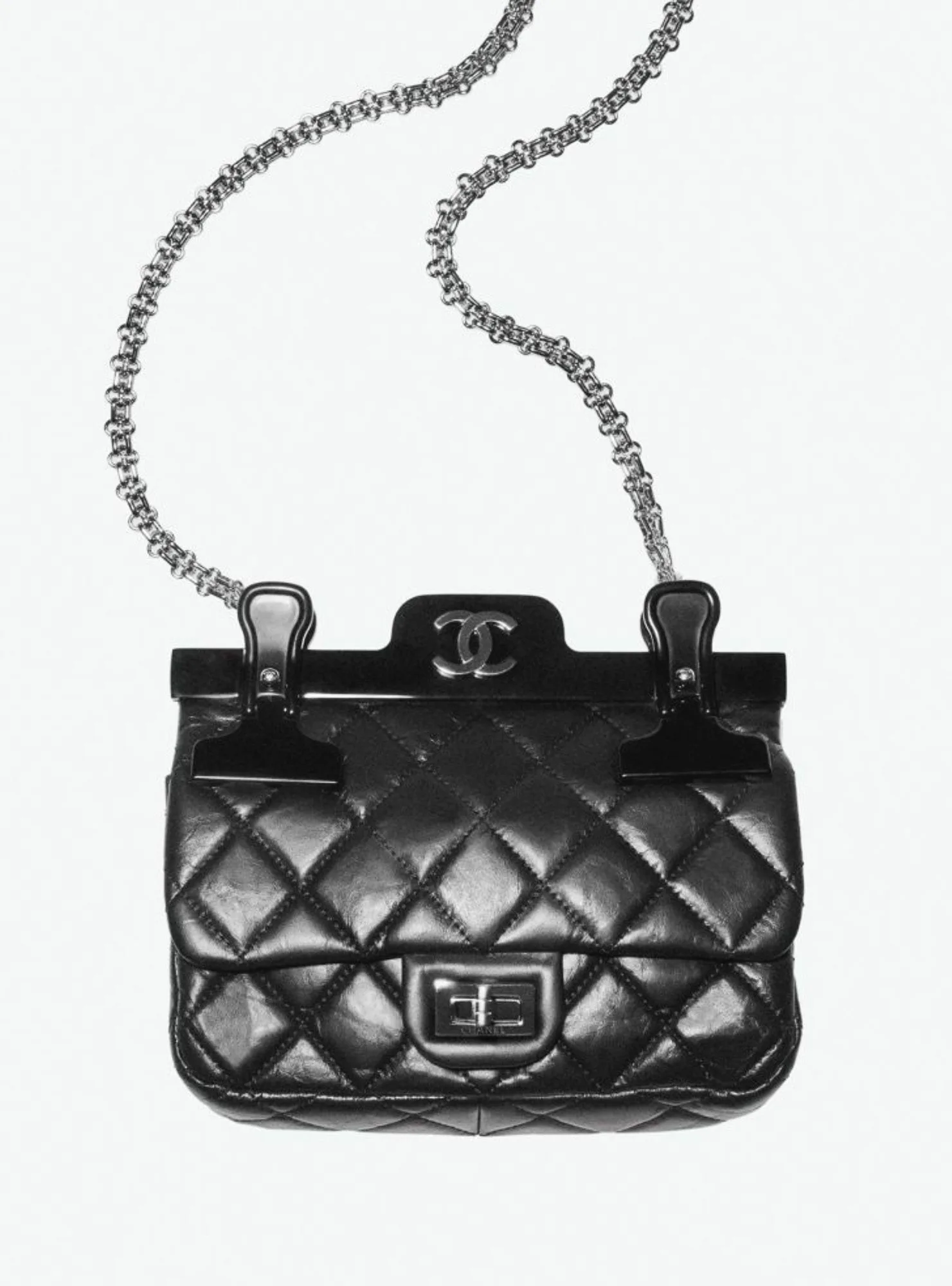 Black quilted leather Chanel bag with silver chain strap and clip hanger on a white background, for Interview Magazine.