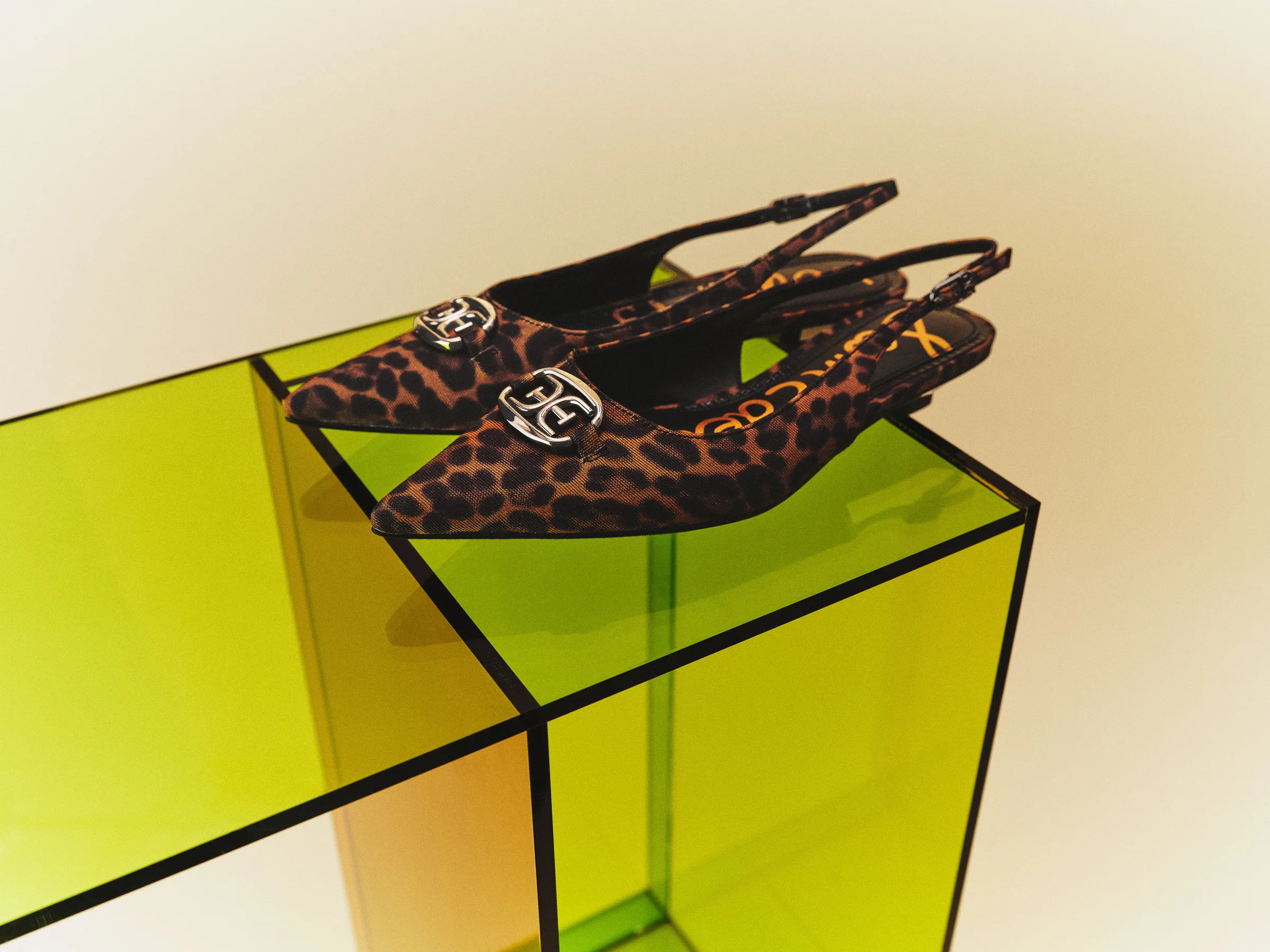 Leopard print slingback flats with silver logo hardware on a lime green acrylic plinth, for Sam Edelman.