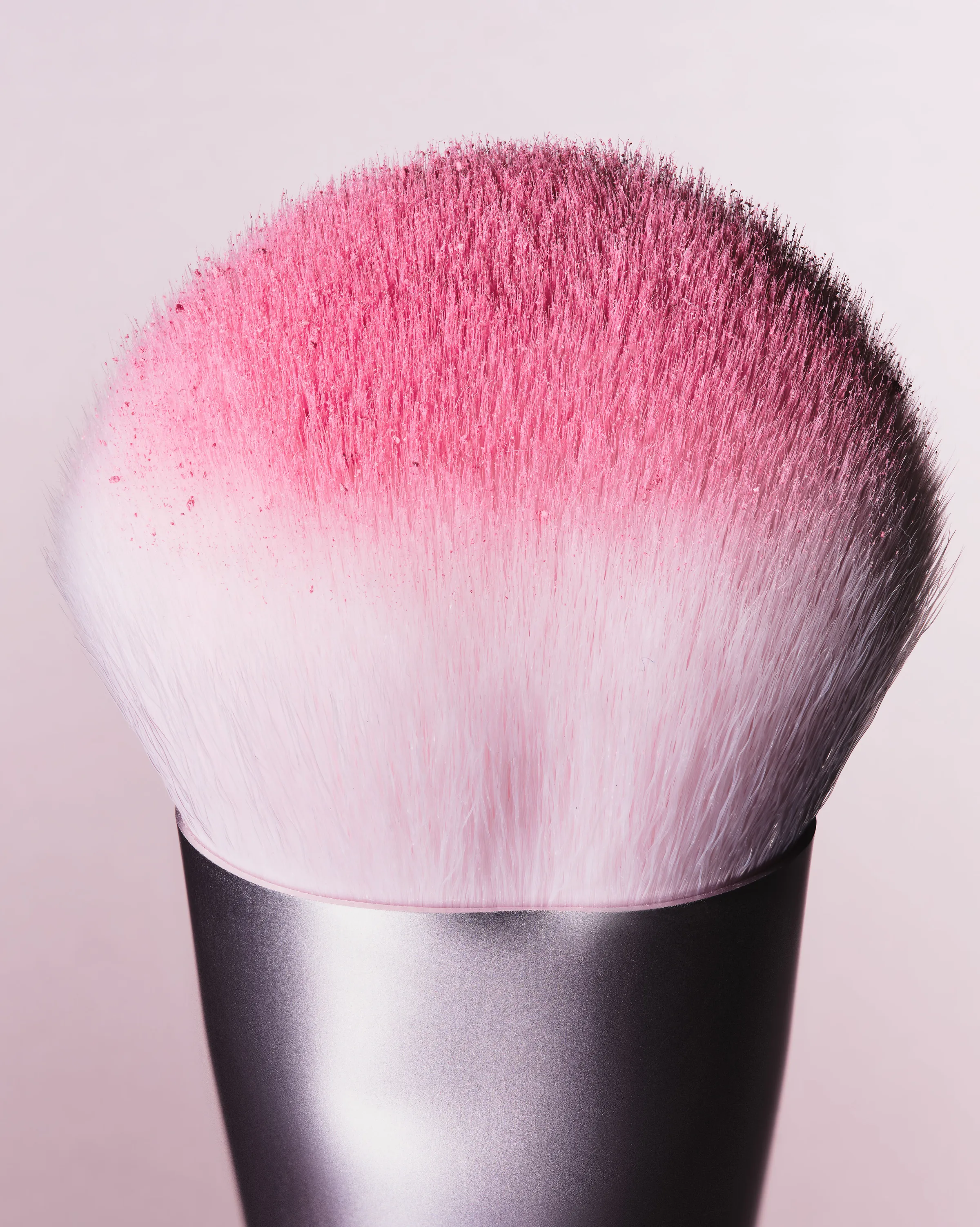 Close-up of a white kabuki brush dusted with pink blush powder on a pale pink background, for Kylie Cosmetics.
