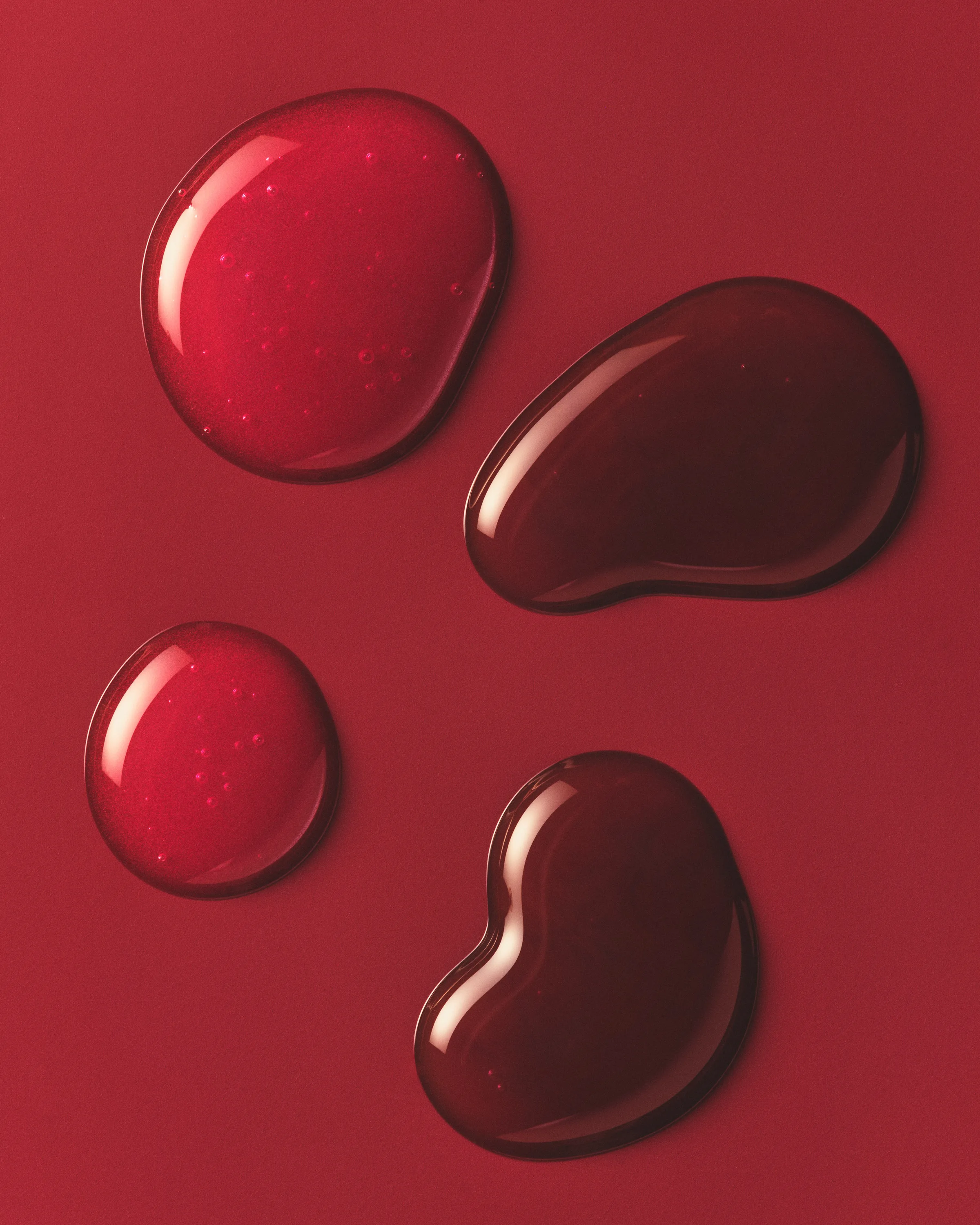 Four glossy red and deep burgundy lip product swatches pooled on a red background, for Kylie Cosmetics.