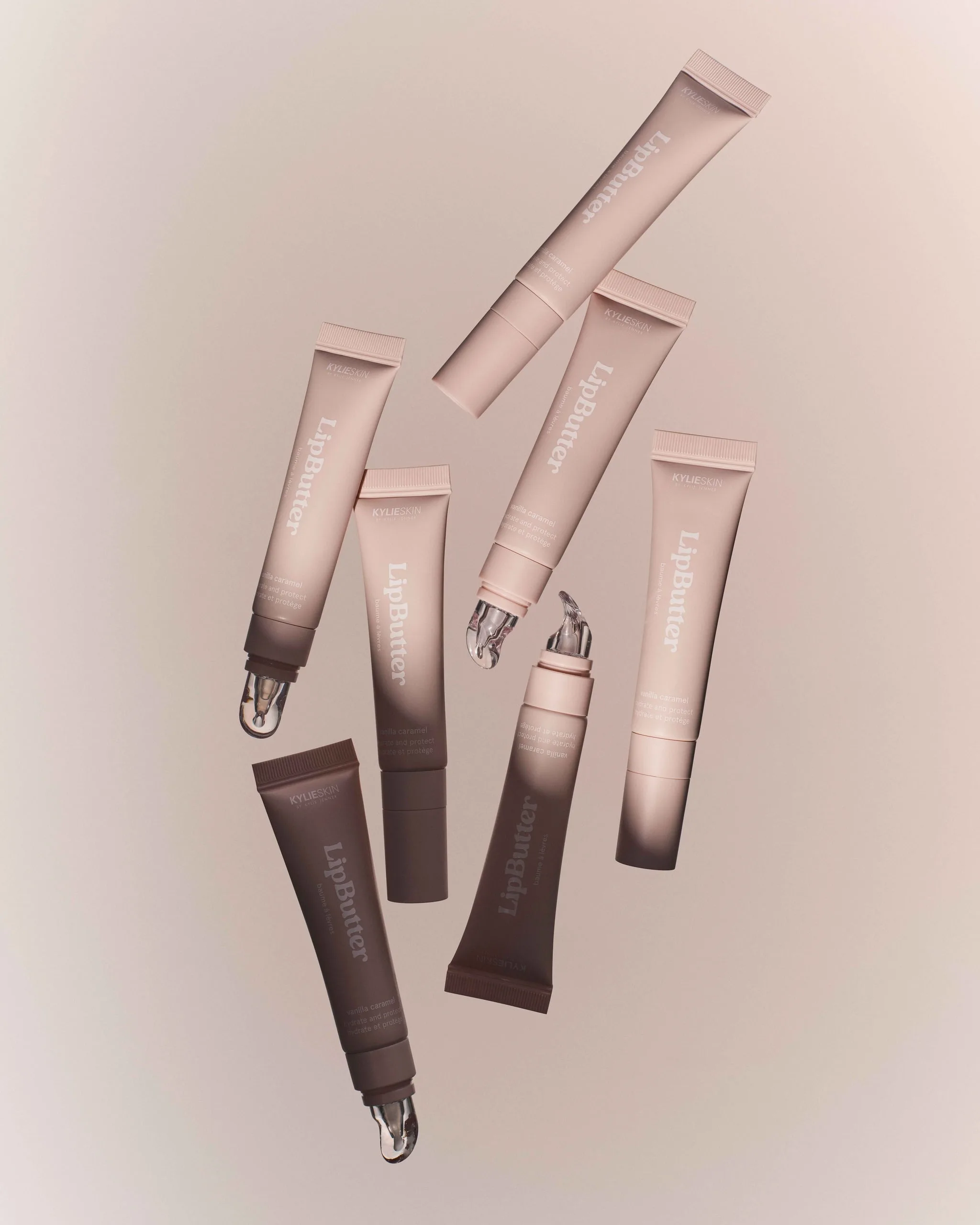 Seven pink and brown Lip Butter tubes floating at angles against a soft blush backdrop, for Kylie Cosmetics.
