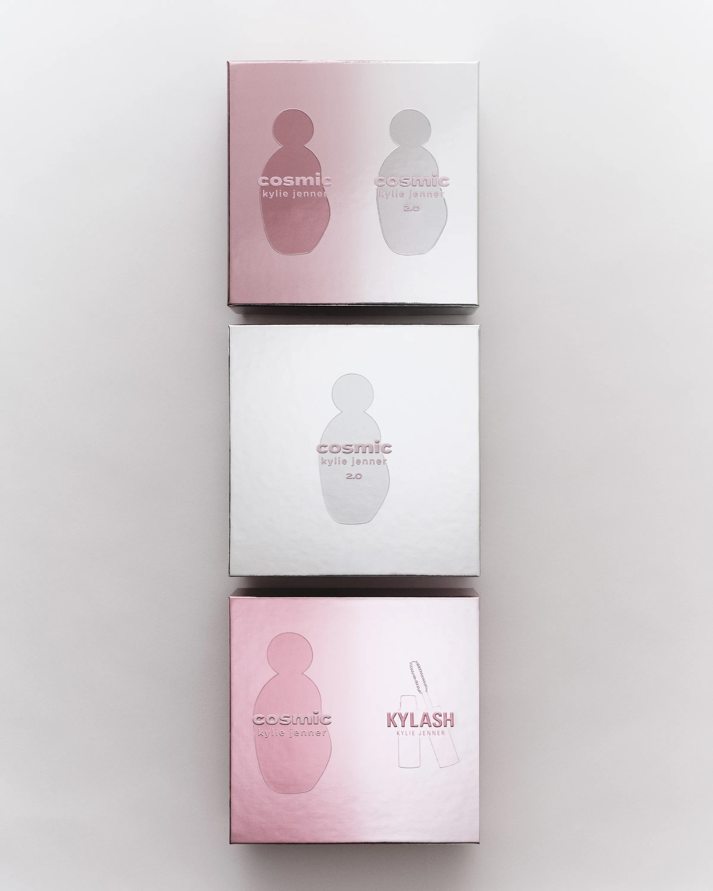 Three pink and silver Cosmic fragrance and Kylash gift boxes stacked vertically on a light grey background, for Kylie Cosmetics.