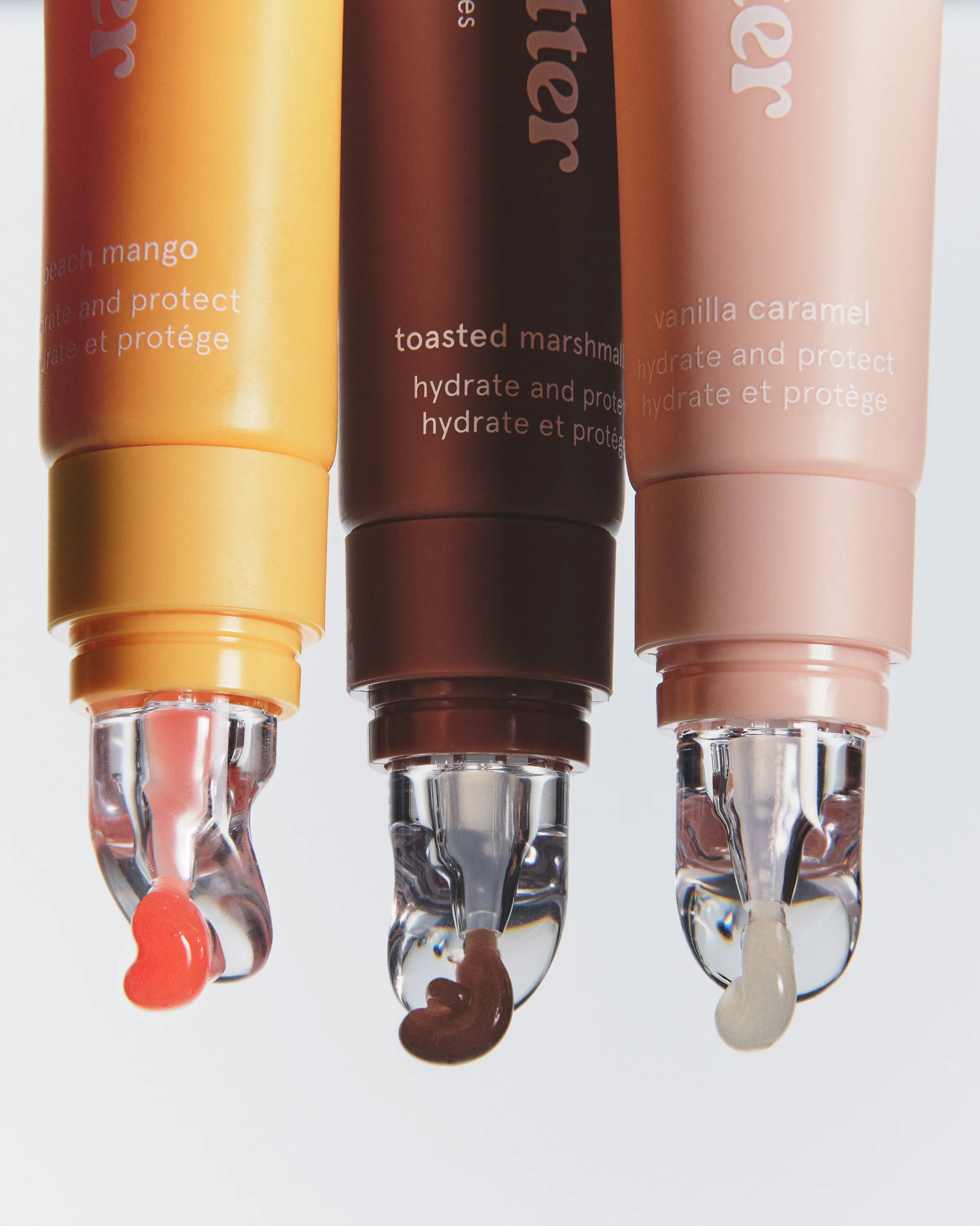 Three lip butter tubes in peach mango, toasted marshmallow and vanilla caramel with product drips, for Kylie Cosmetics.