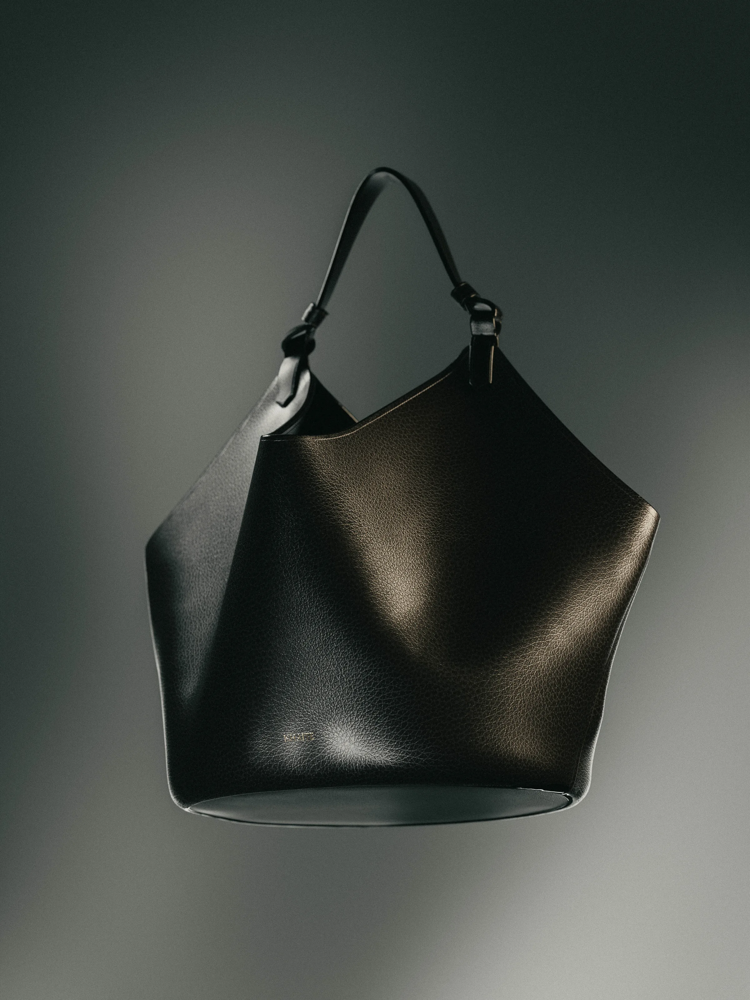 CGI render of a black pebbled leather bucket bag with knotted top handle, floating against a grey backdrop, for Khaite.
