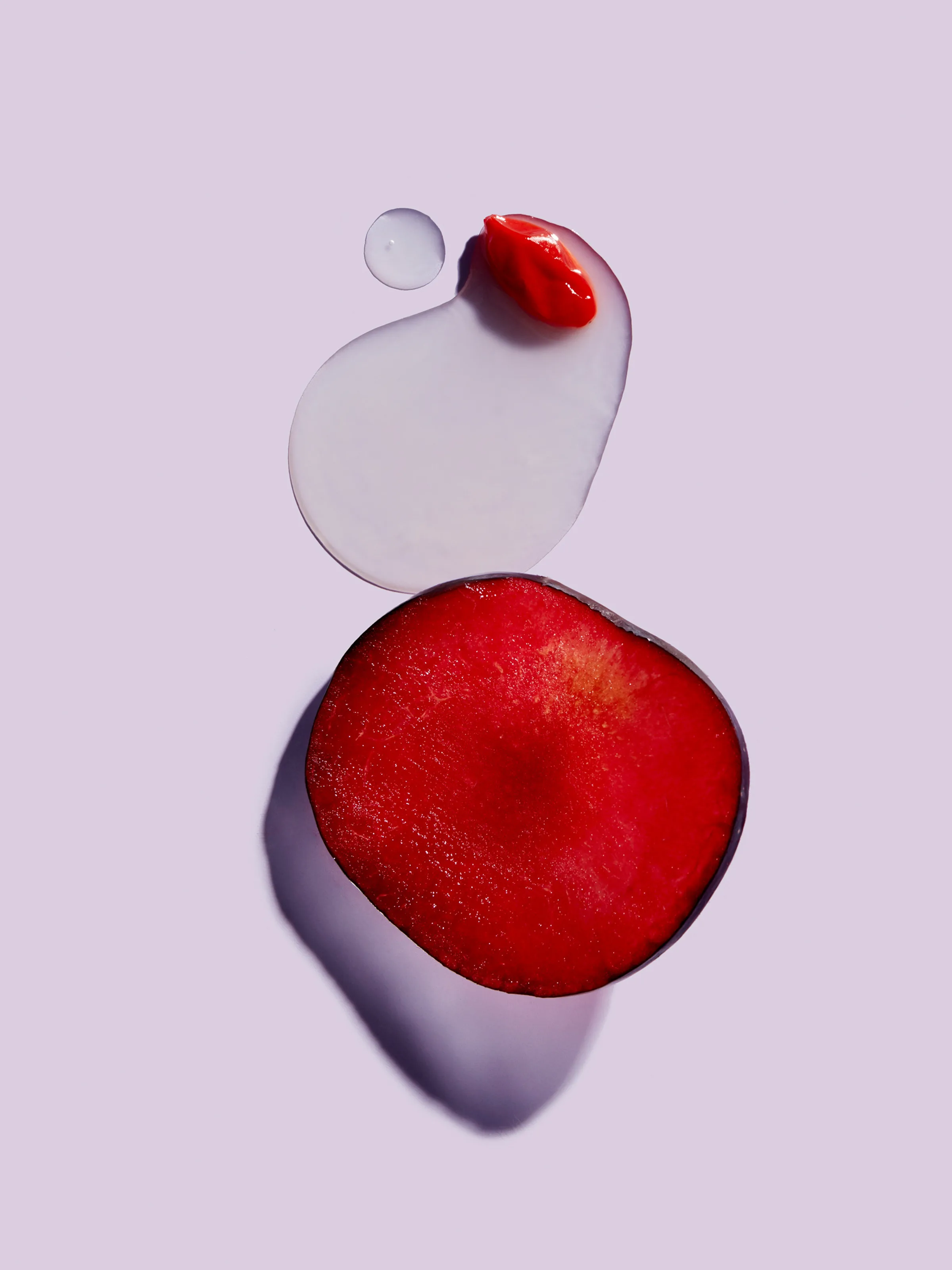 Sliced red plum beside a clear serum pool and red cream swatch on a lilac background, for Erno Laszlo.