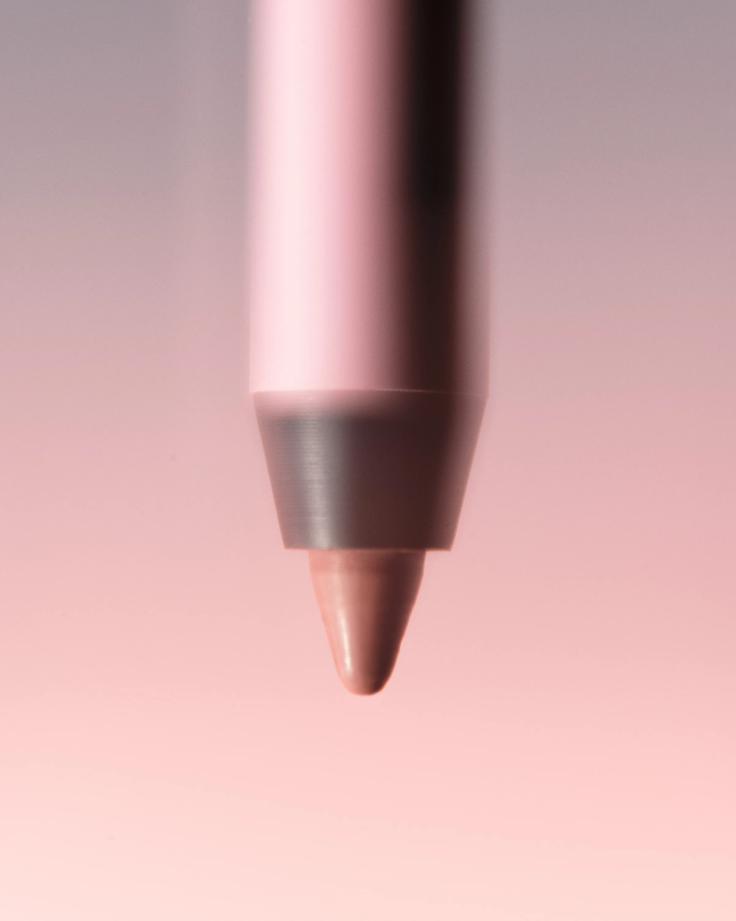 Close-up of a pink lip liner pencil tip in a nude coconut shade against a soft pink gradient, for Kylie Cosmetics.