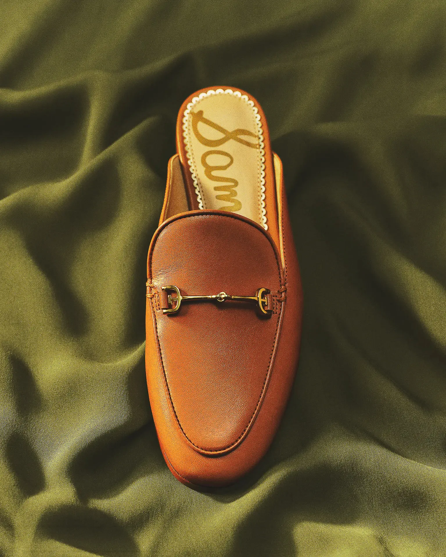 Tan leather loafer mule with gold horsebit hardware on draped olive green satin, for Sam Edelman.